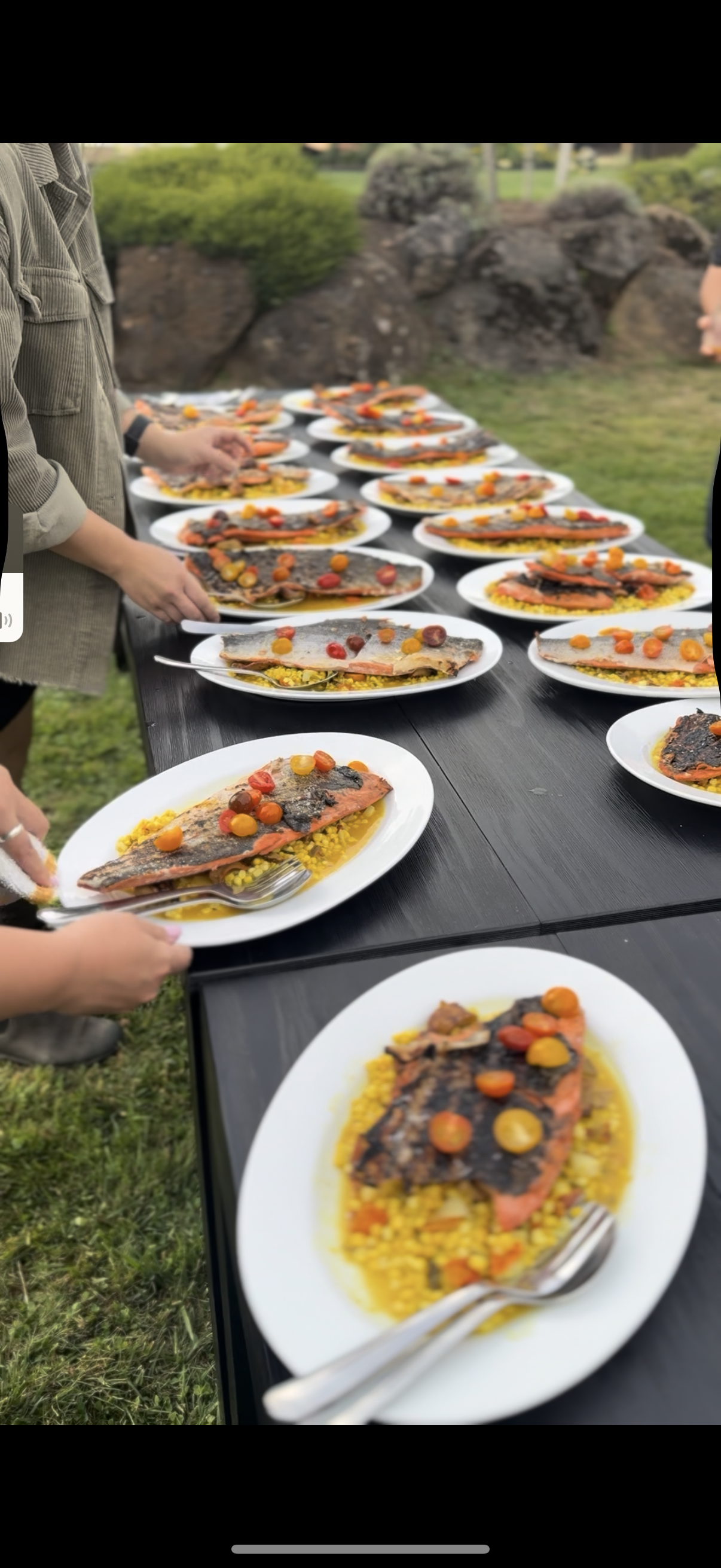 Plates of grilled salmon with cherry tomatoes and yellow rice on a long outdoor table.