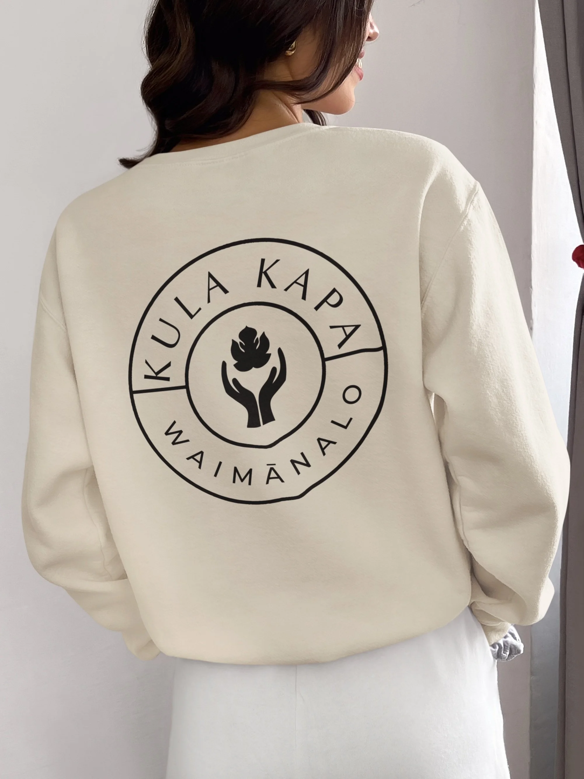 Woman in cream-colored sweatshirt showing back with black logo and text 'KULUA KAPA Waimānalo'