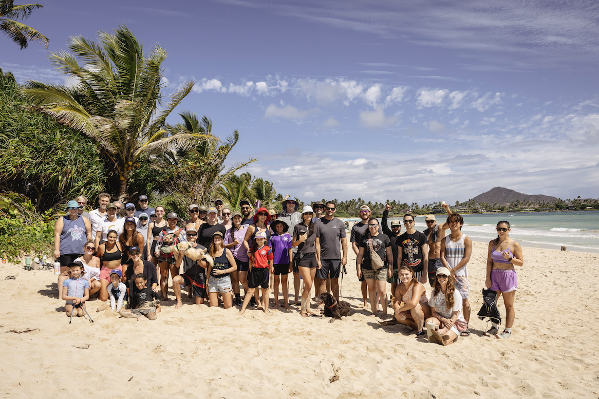 Group of people and children on a beach with palm trees and ocean in the background, sunny day with scattered clouds.