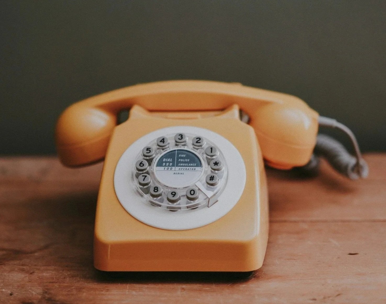 Vintage orange rotary dial telephone on a wooden surface.