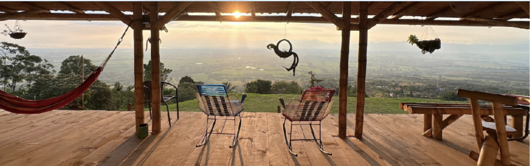 A spacious wooden deck with outdoor chairs, a hammock, and hanging planters overlooking a scenic valley at sunset.