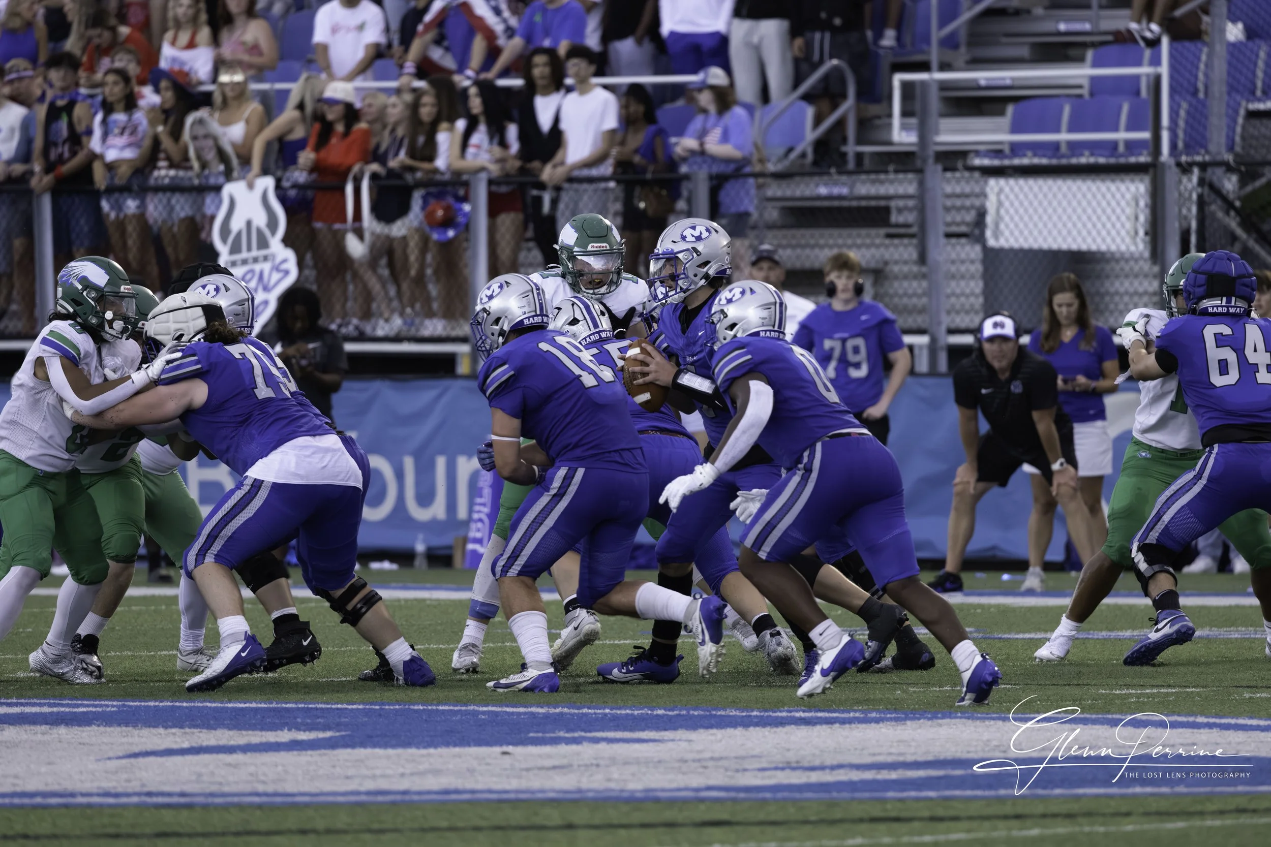 Football game with players in blue and white uniforms, on a field with spectators in the background.