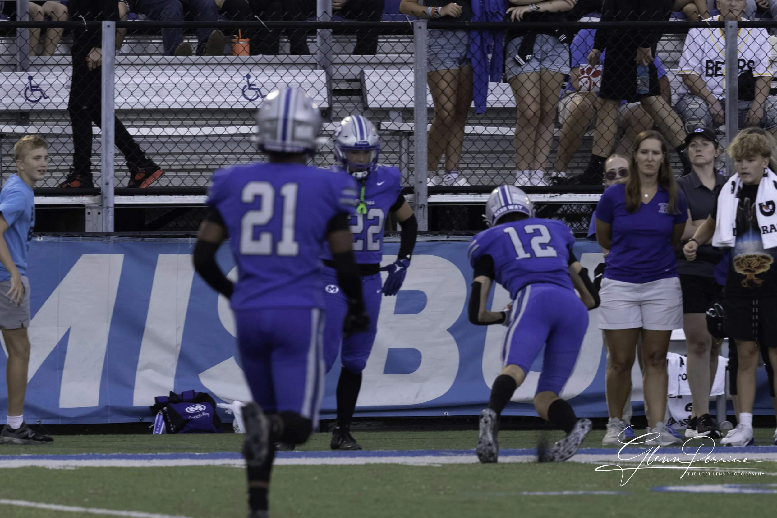 American football players in blue uniforms celebrating on the sidelines, with spectators in the background.