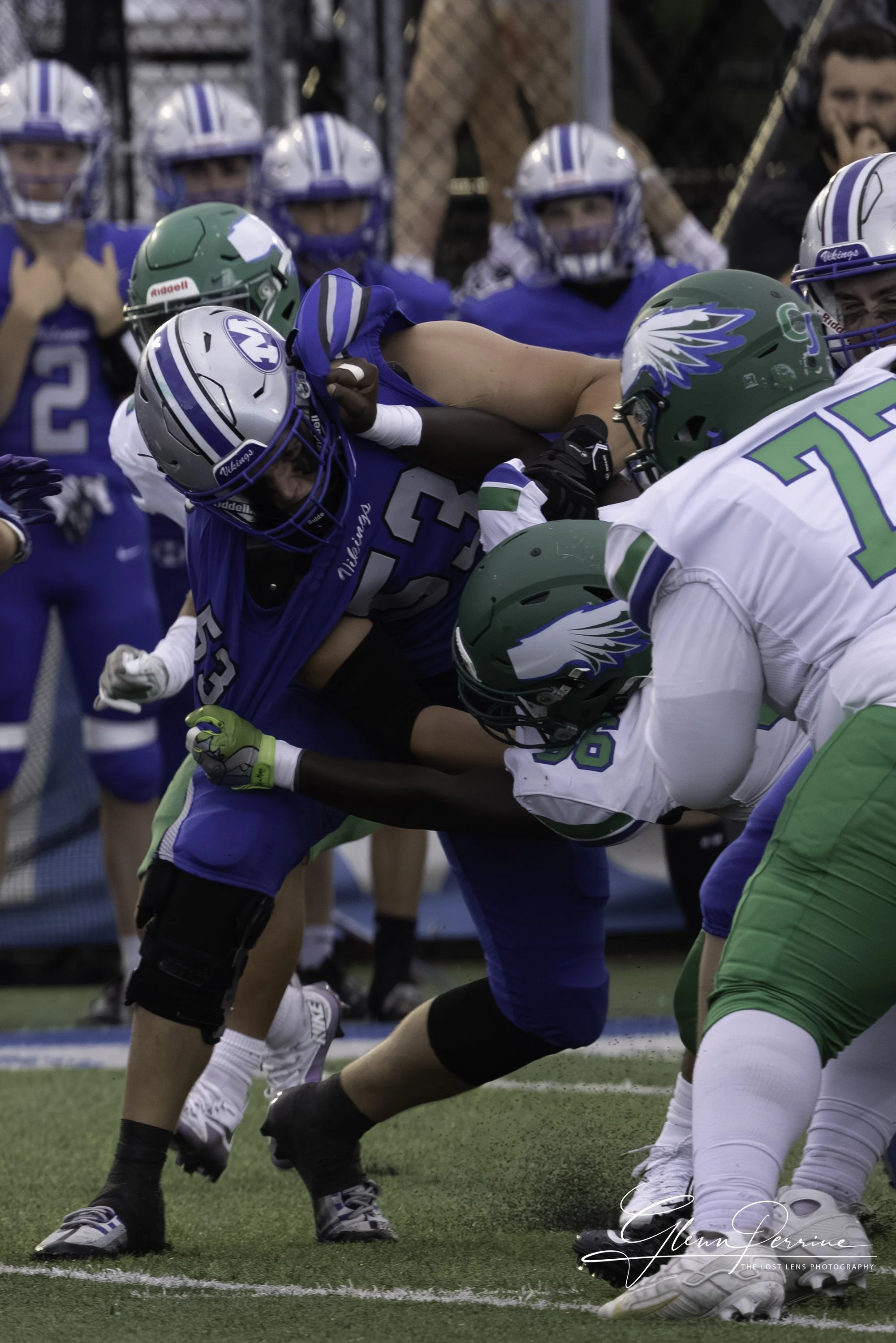 Football players in blue and green uniforms engaged in a tackle during a game.