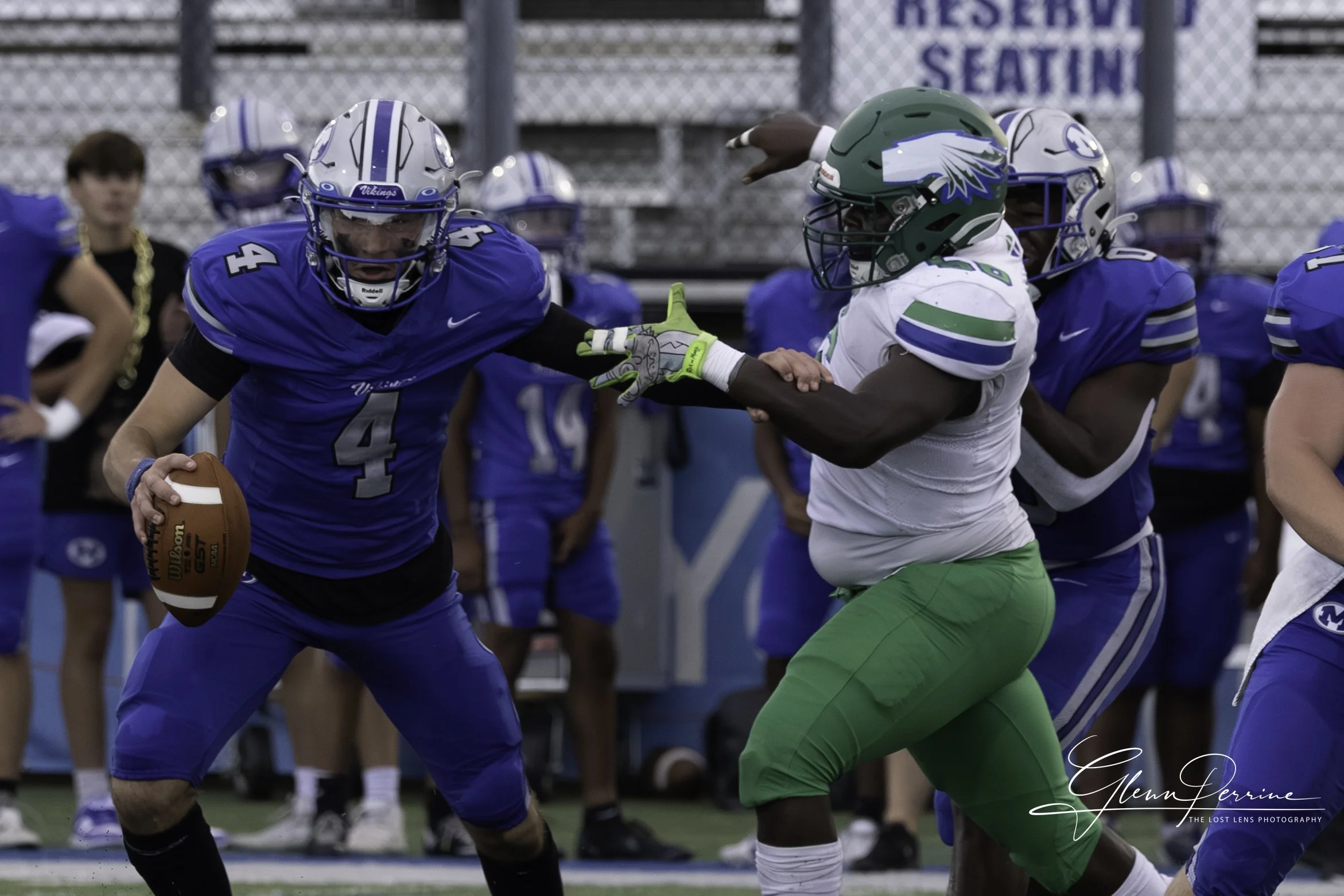 Football player in blue uniform running with the ball while being impeded by a player in green and white uniform during a game.