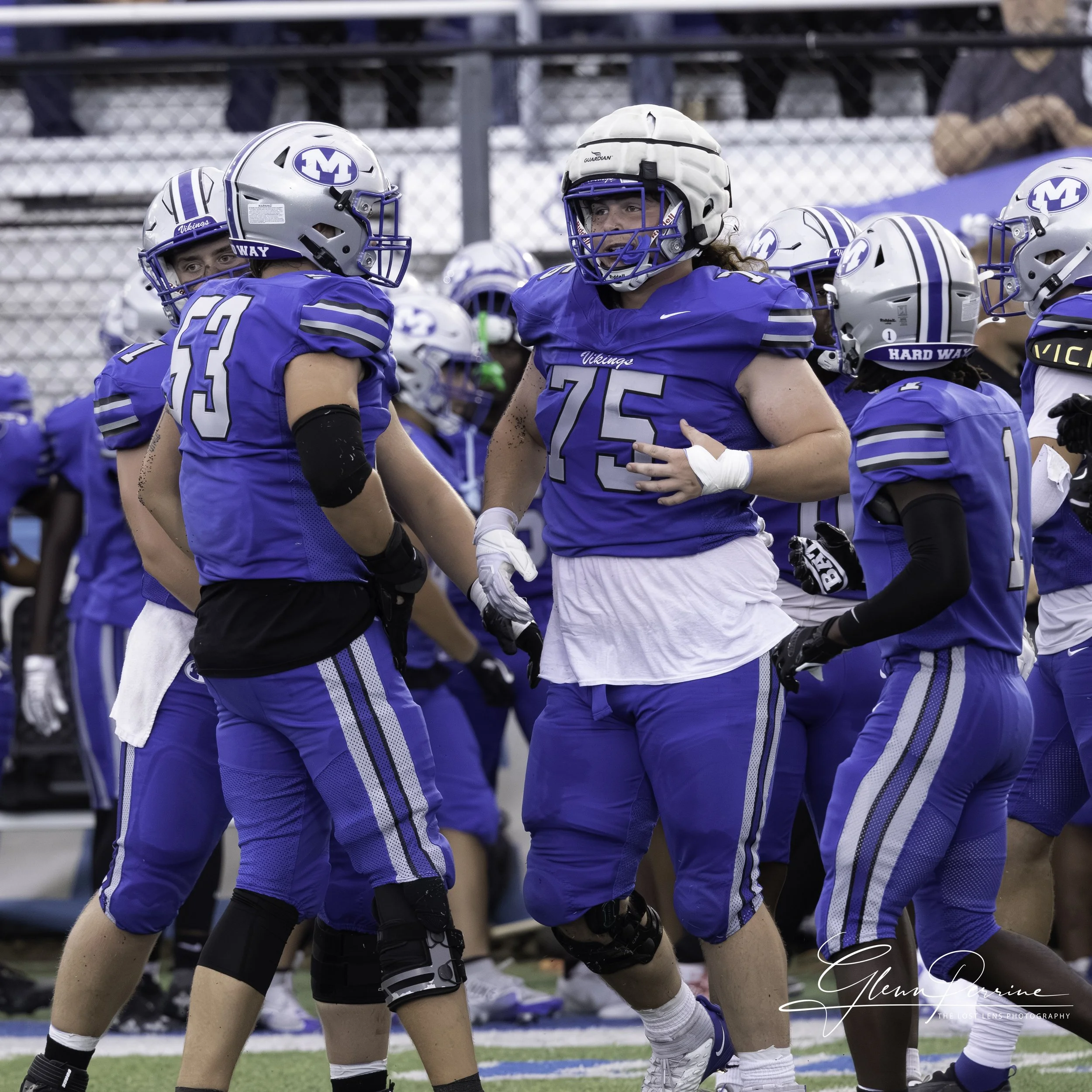 Football players in blue and white uniforms celebrating on the field, wearing helmets and pads.