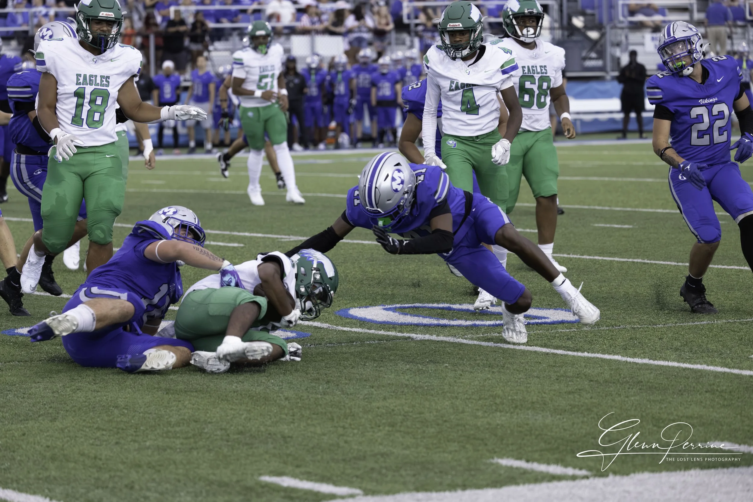 Football players from the Eagles and Vikings teams compete on the field, with a player in black and blue attempting to advance the ball, while other players surround him during a game.