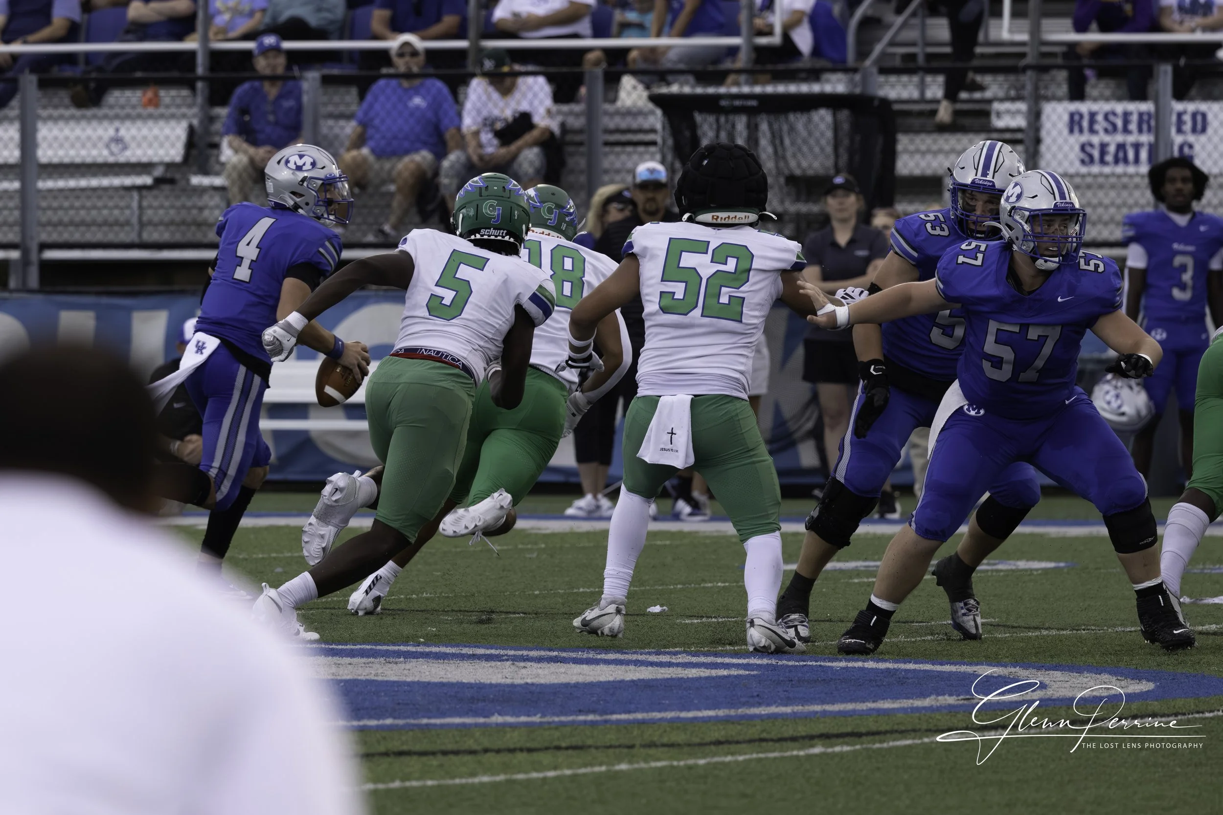 University of Kentucky football players in white and green uniforms running with the ball, opposing Michigan players in blue uniforms trying to block or tackle on the field during a game.
