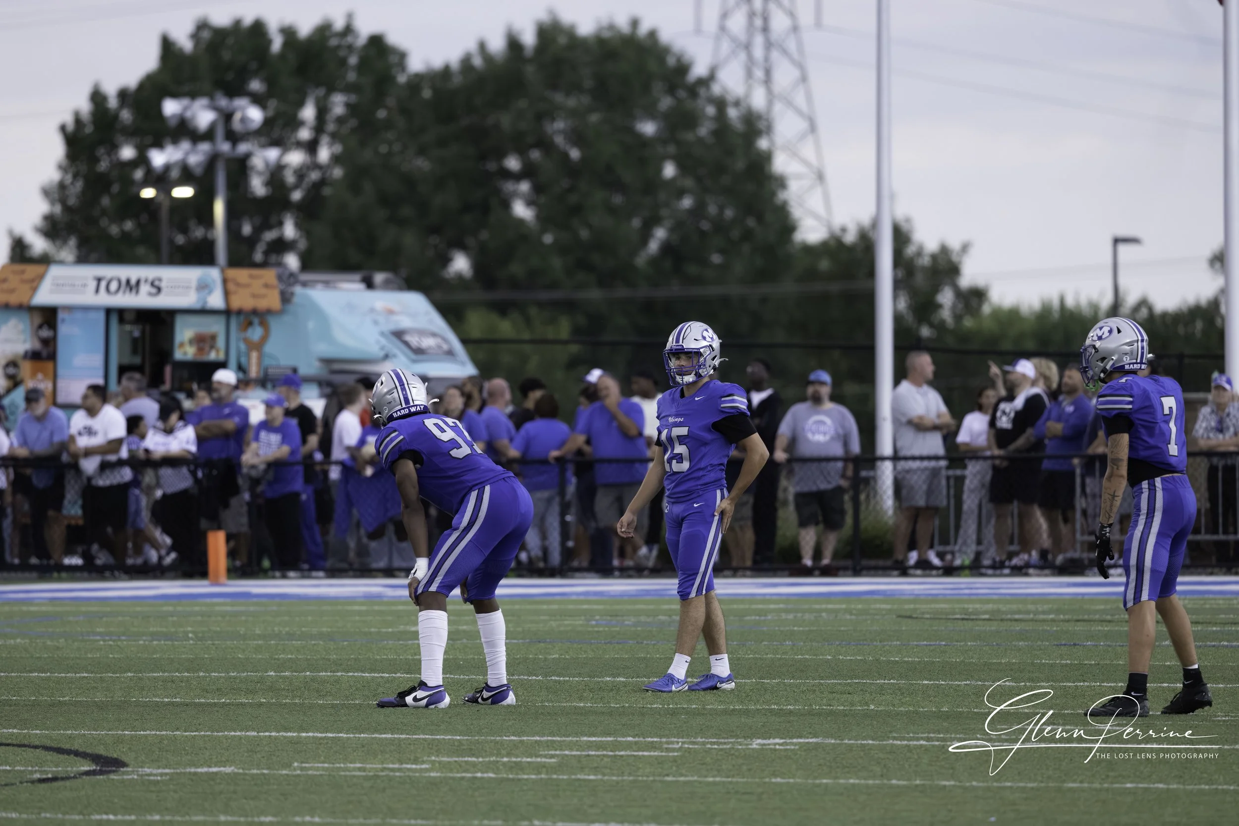 A football game in progress with players in blue uniforms on the field and spectators watching from the sidelines.