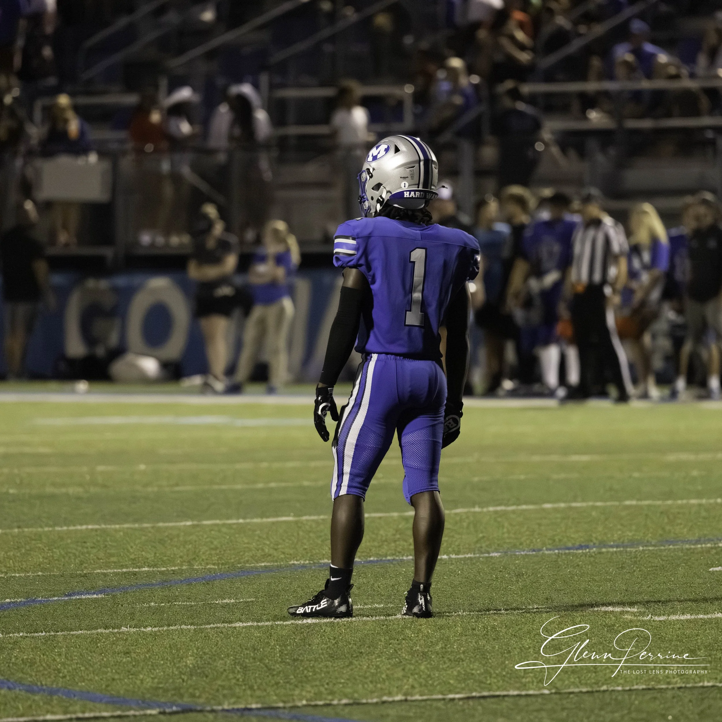American football player wearing a blue uniform with the number 1, standing on the field with a crowd in the background.