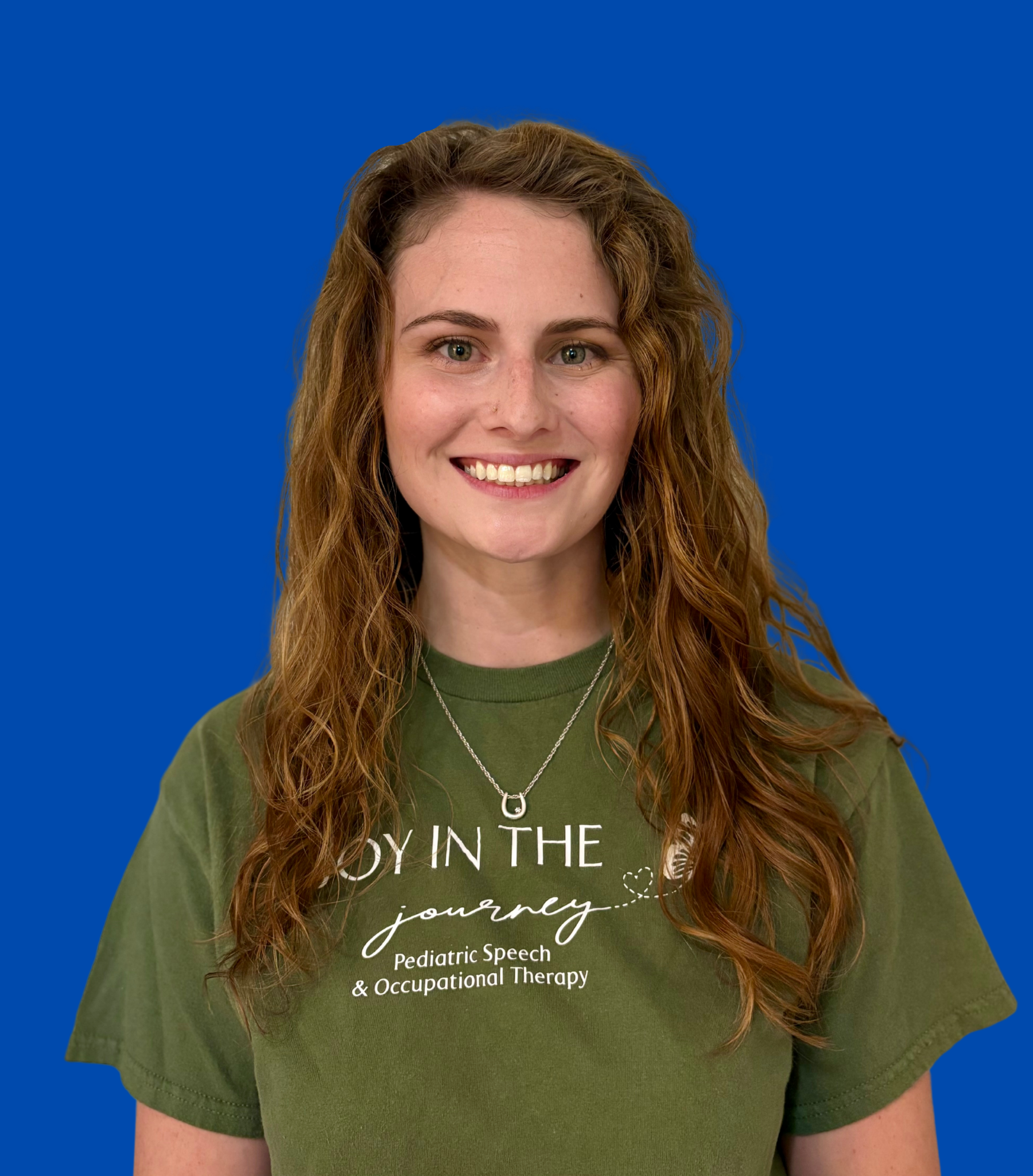 Young woman with long curly hair, smiling, wearing a green T-shirt with text and butterfly graphic, against a solid blue background.
