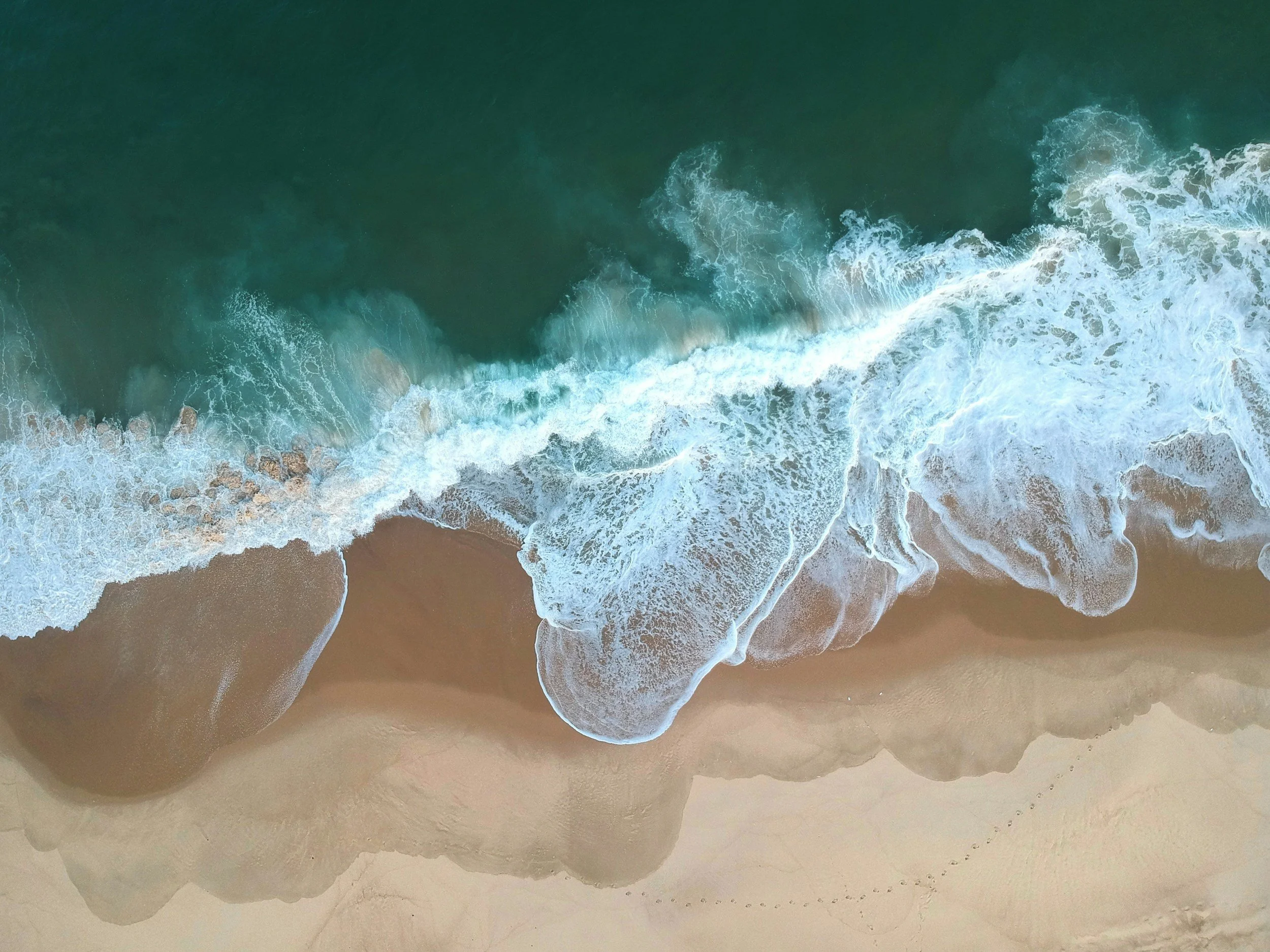 An aerial view of ocean waves crashing onto sandy beach shoreline.