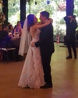 A bride and groom dancing at their wedding reception, surrounded by guests in a decorated venue.