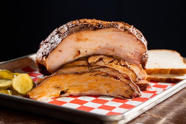 Slices of smoked turkey breast on a tray with pickles and bread.