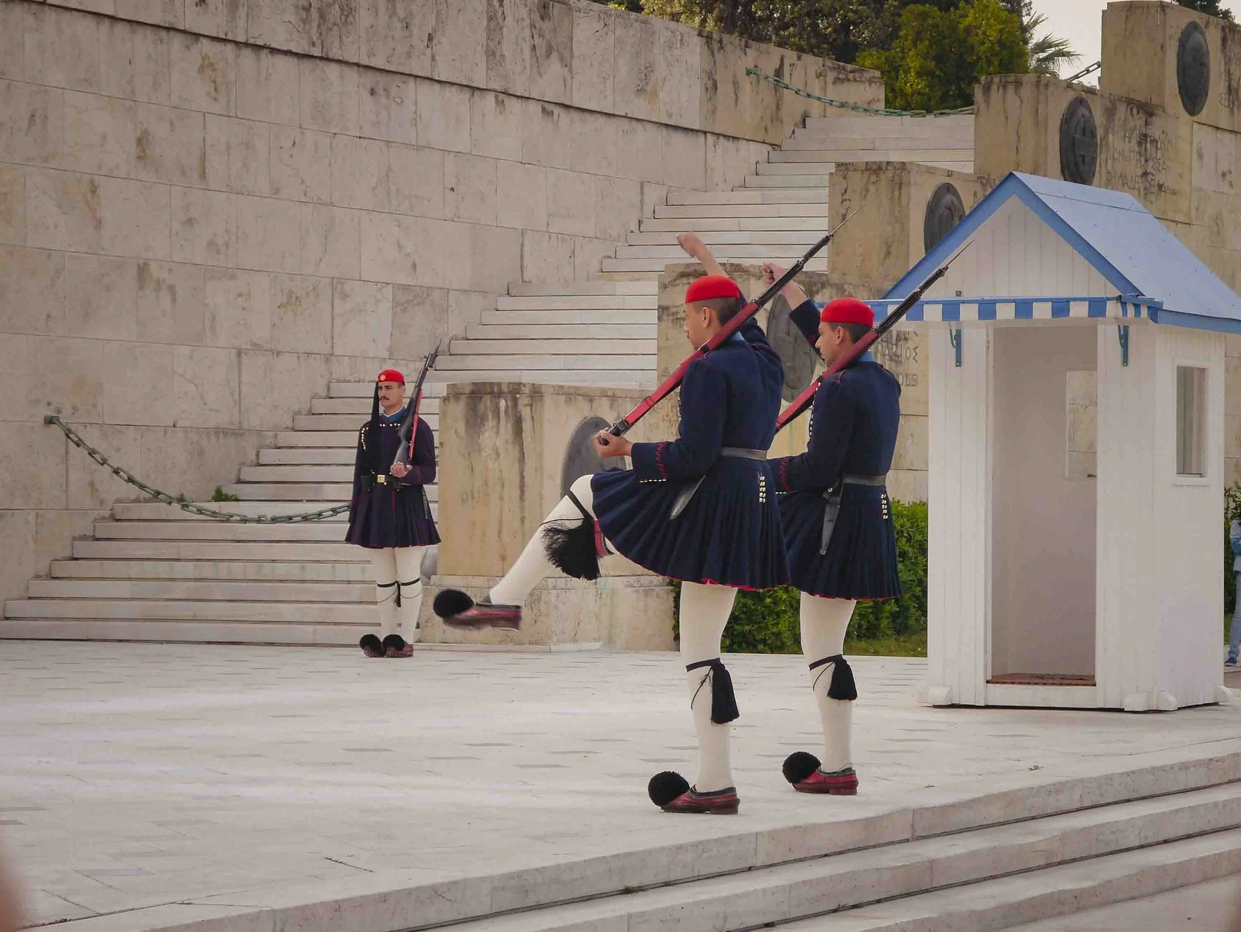 Evzones Presidential Guards in traditional uniform performing the ceremonial changing of the guard at the Tomb of the Unknown Soldier in Athens' Syntagma Square, showcasing their distinctive synchronized movements.