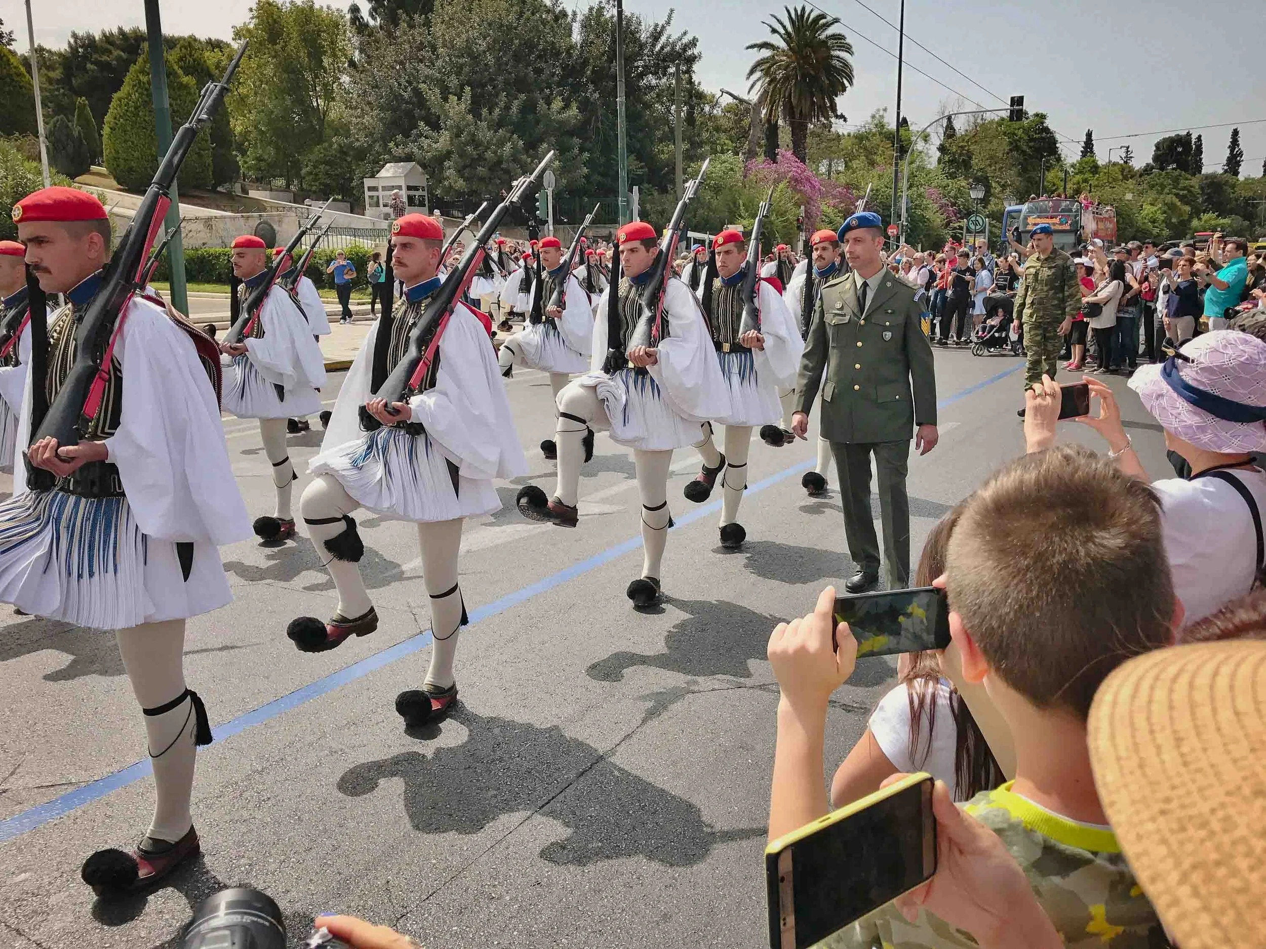 Evzones Presidential Guard parade in full ceremonial dress marching through Athens streets with crowds of tourists watching and photographing the traditional Greek military ceremony.
