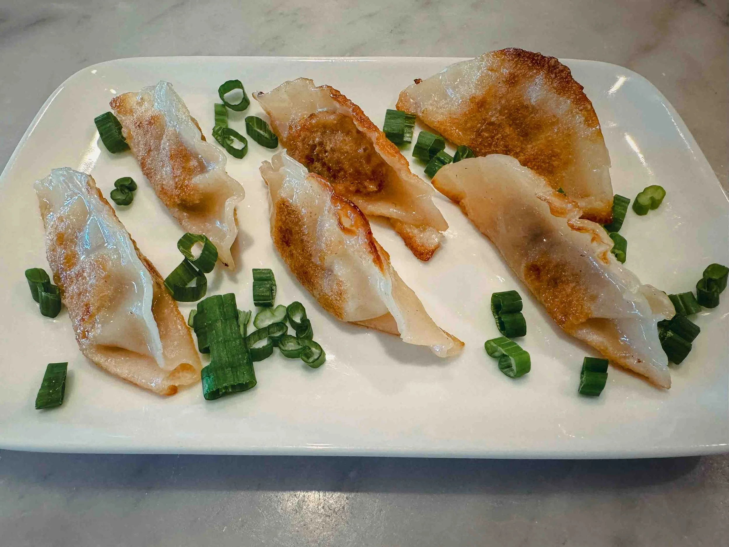Finished Chinese pot stickers arranged on a white rectangular plate with golden-brown crispy bottoms, translucent steamed tops, and fresh scallion garnish, ready to serve with dipping sauce