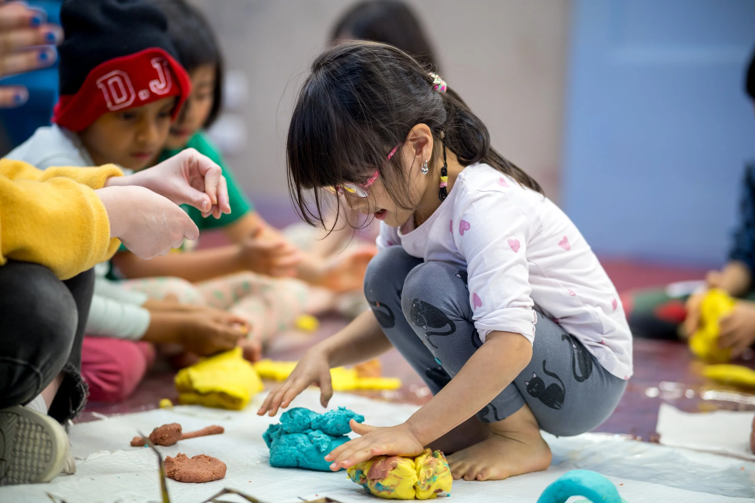 Children sitting on the floor, playing with colorful clay or play dough.