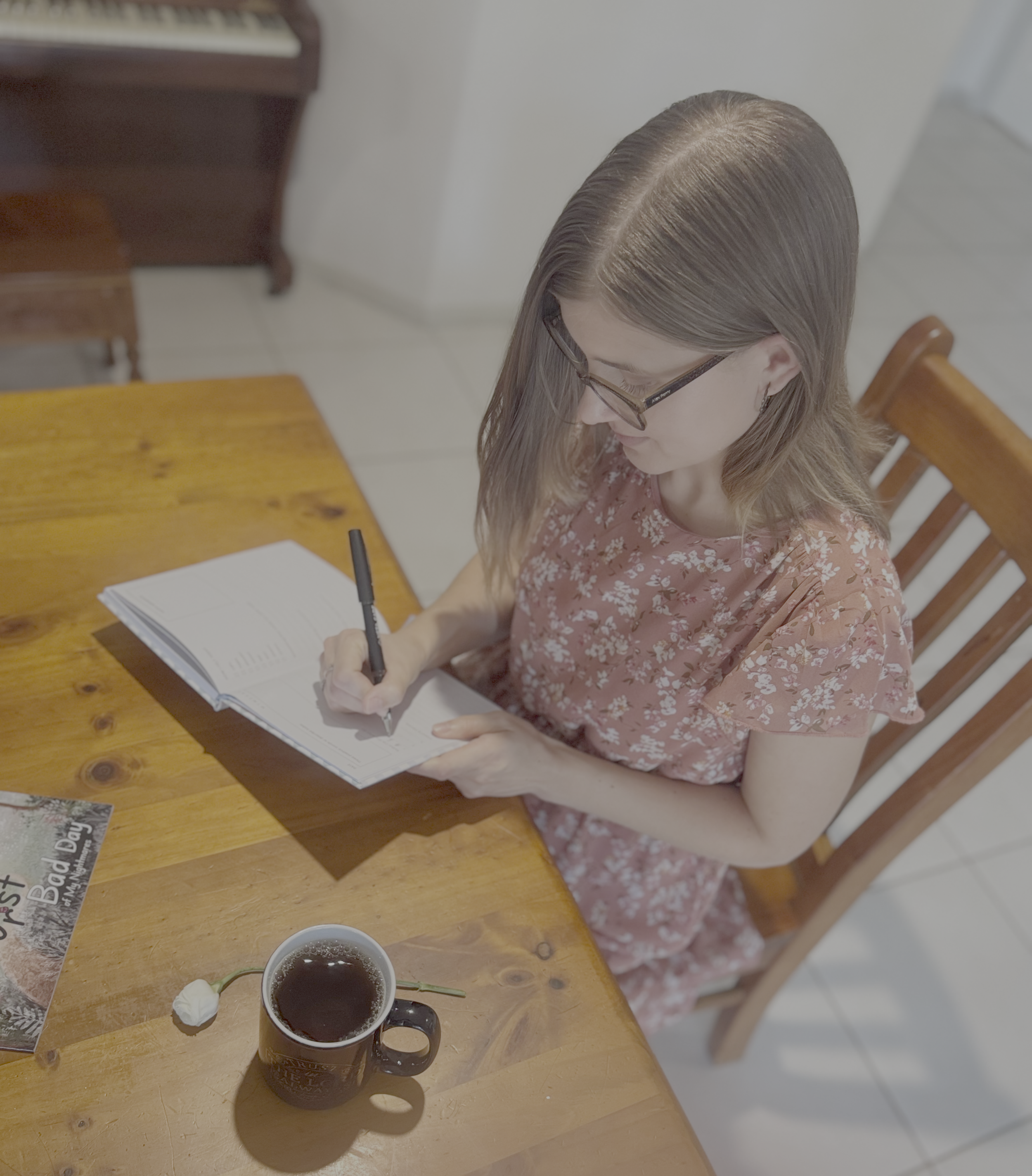 Courtney sits at a table with a cup of tea and book, writing in a journal
