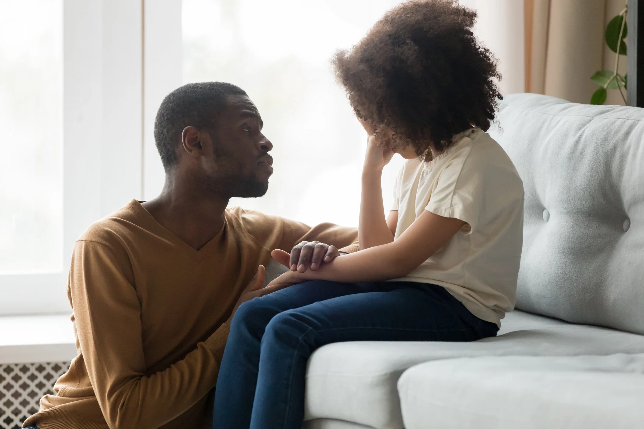 Man comforting a child on a couch indoors, engaging in a supportive conversation.