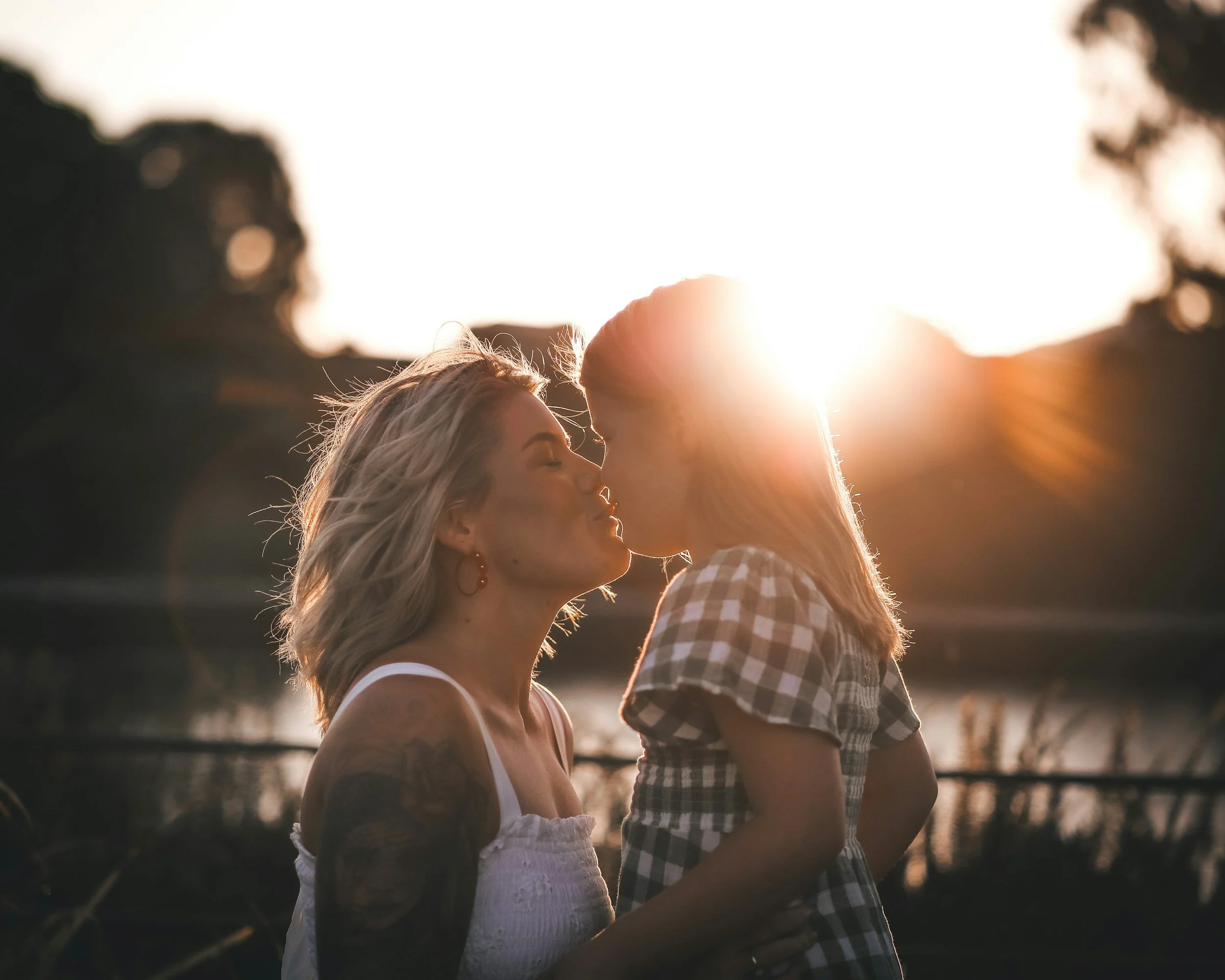 Two women kissing at sunset outdoors.