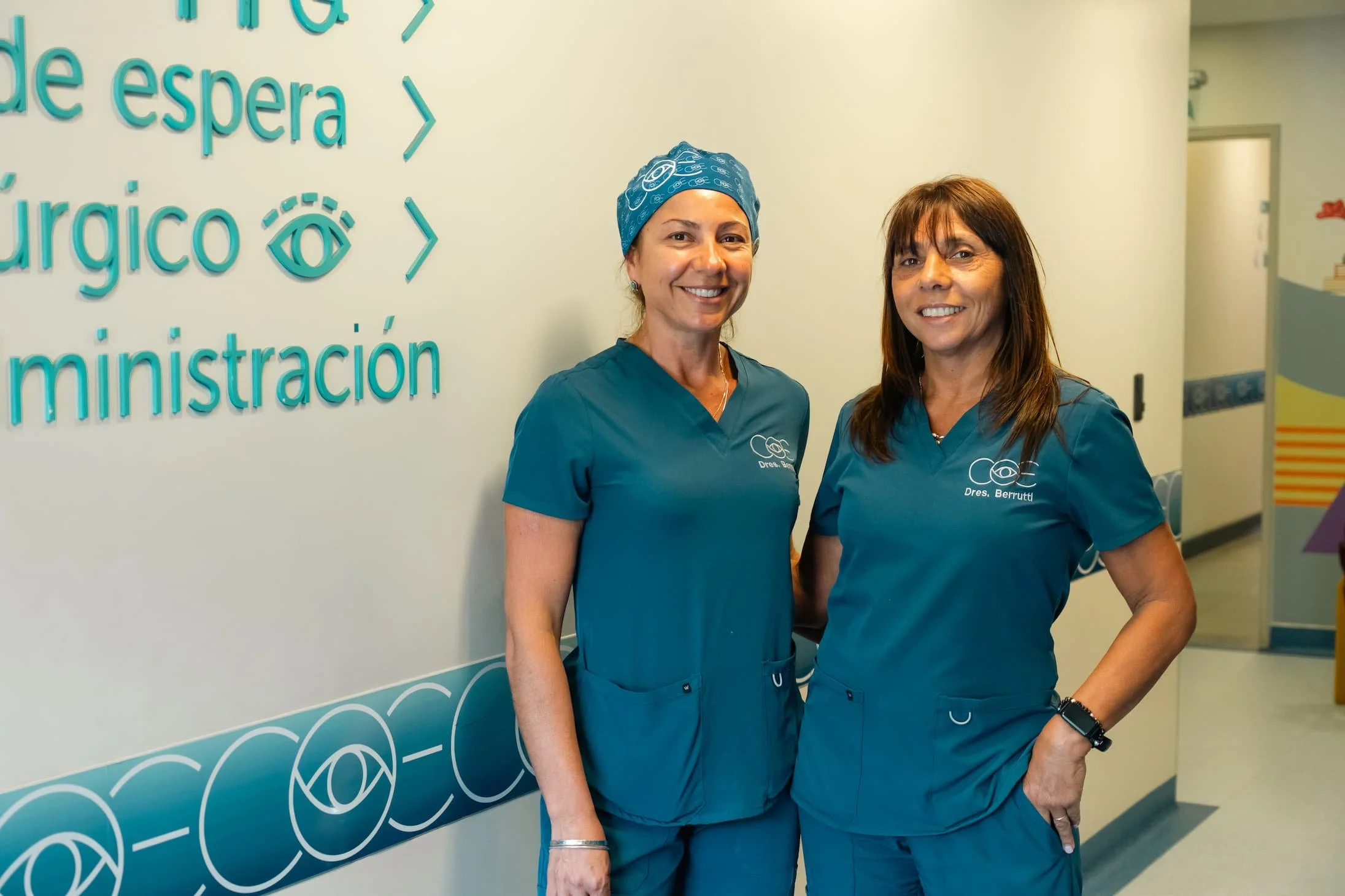 Profesionales con uniforme médico en un hospital, de pie junto a una pared con texto en español relacionado con cirugía y espera.