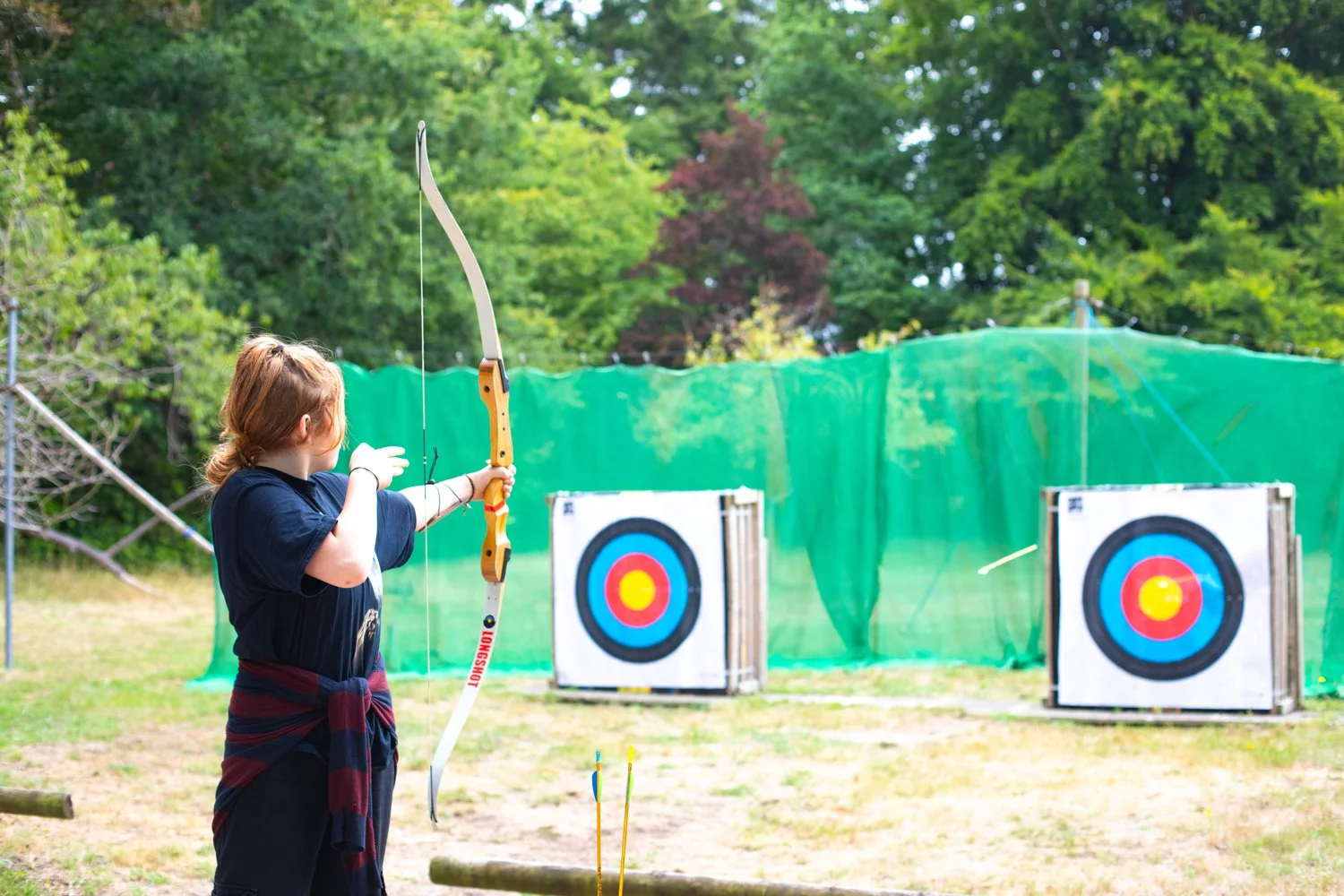 Two archers aiming at targets outdoors, with bows drawn.