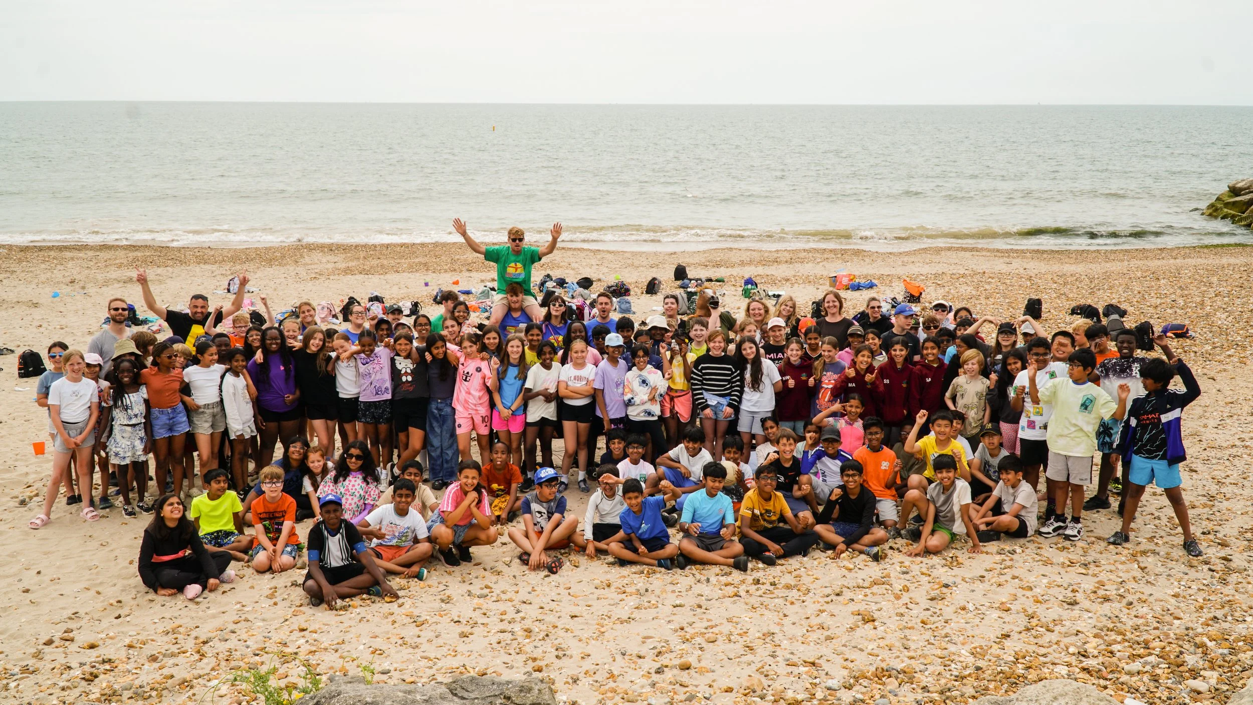 A large group of children and adults on a beach posing for a group photo with the sea in the background.