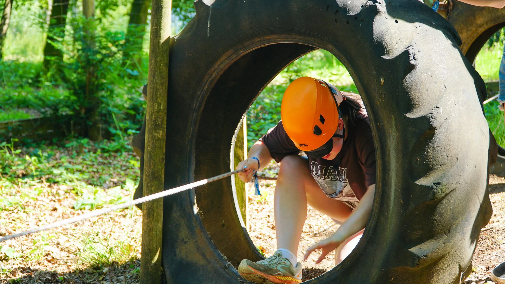 Children wearing blindfolds, holding onto a rope, and navigating an outdoor Nightline obstacle course together.