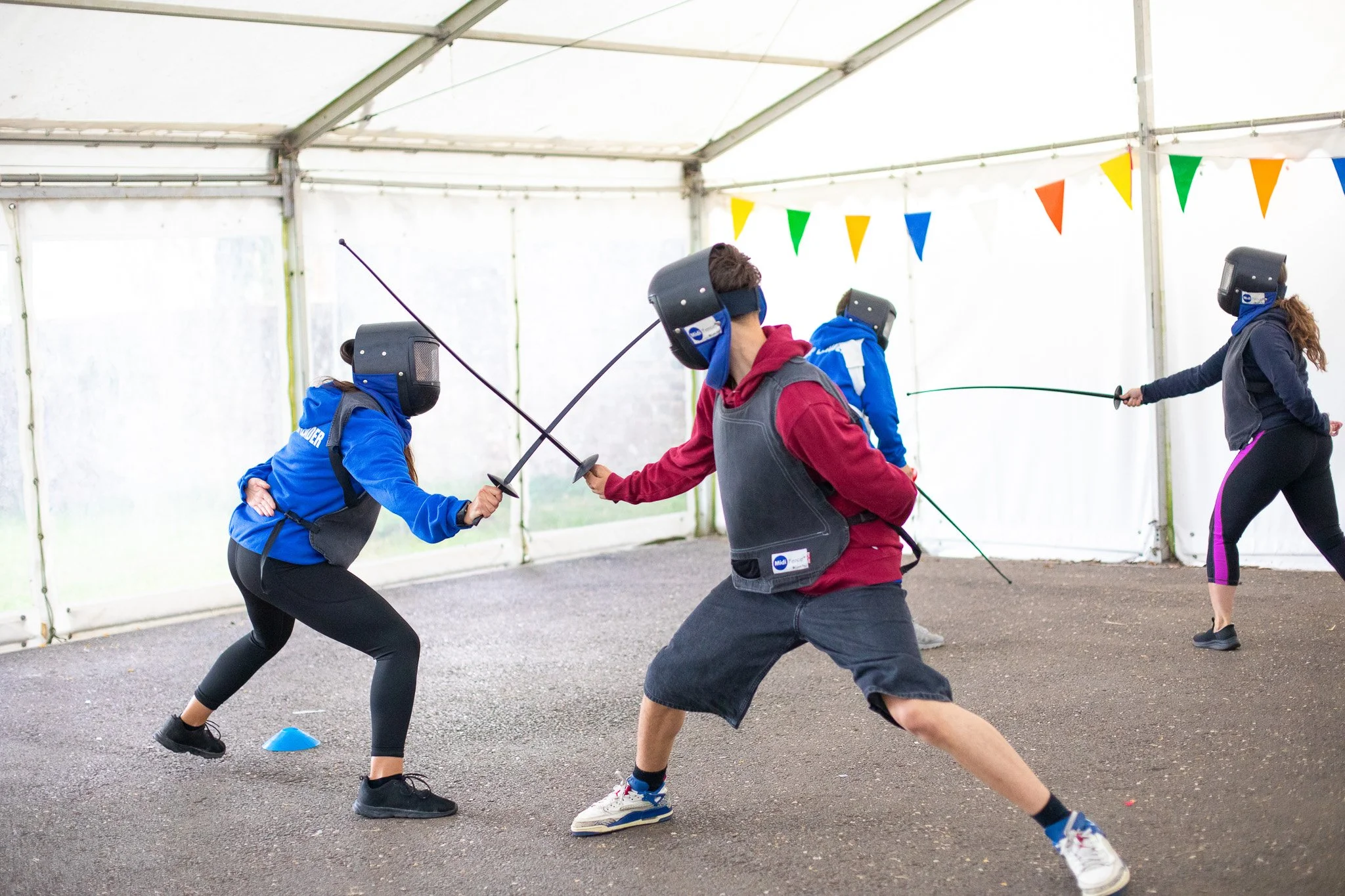 Child in protective fencing gear practicing footwork and sparring with an instructor outdoors.