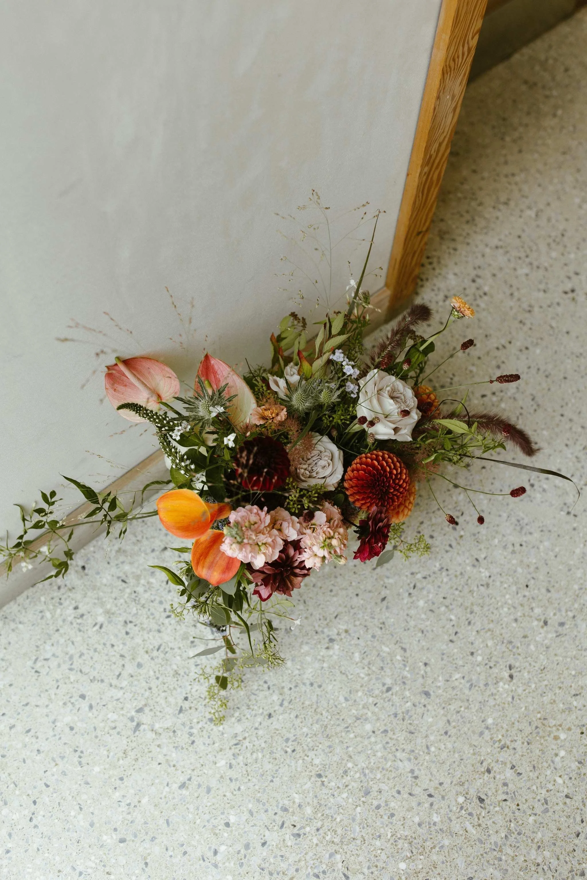 A colorful flower arrangement placed on a speckled beige floor next to a wooden wall.