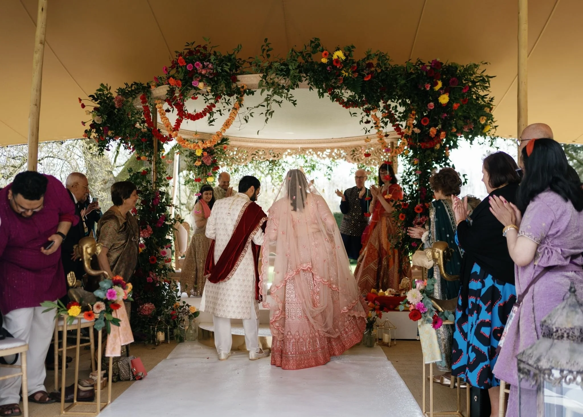 A wedding ceremony with a bride and groom standing under a floral arch, surrounded by guests.