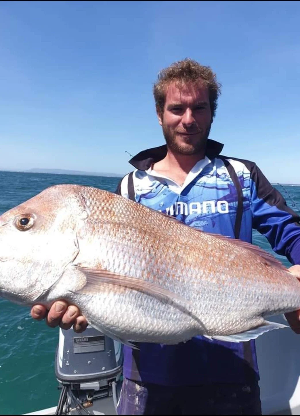 Man holding a large red snapper fish on a boat in the ocean during sunny weather.
