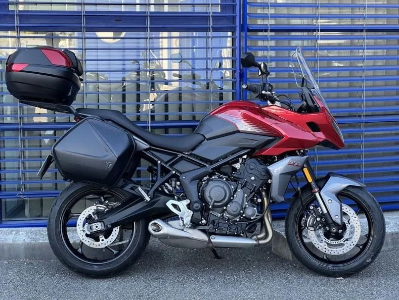 Red and black touring motorcycle with side and rear storage parked in front of a blue metal fence.