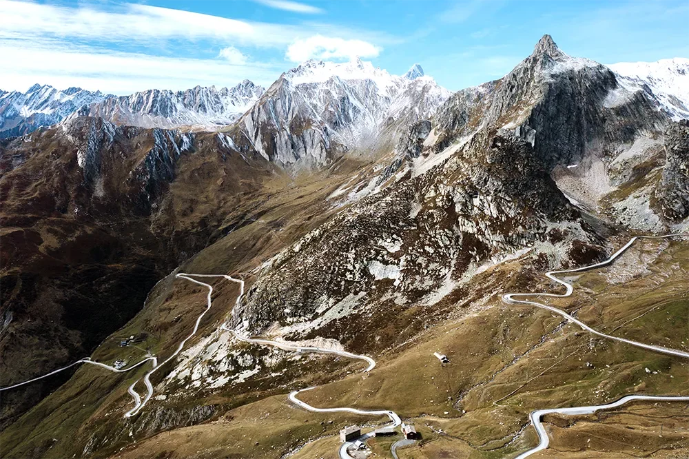 Winding mountain road through alpine landscape with rugged peaks and snow-capped summits.