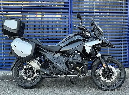 Black adventure motorcycle with side cases and top case parked in front of a blue metal fence.