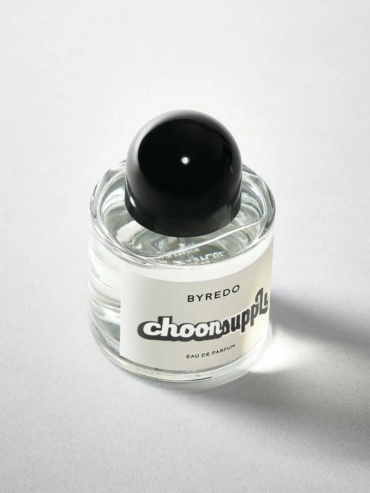 A small, clear perfume bottle with a white label that says 'BYREDO choonsoople Eau de Parfum,' topped with a shiny black cap, placed on a plain white surface.