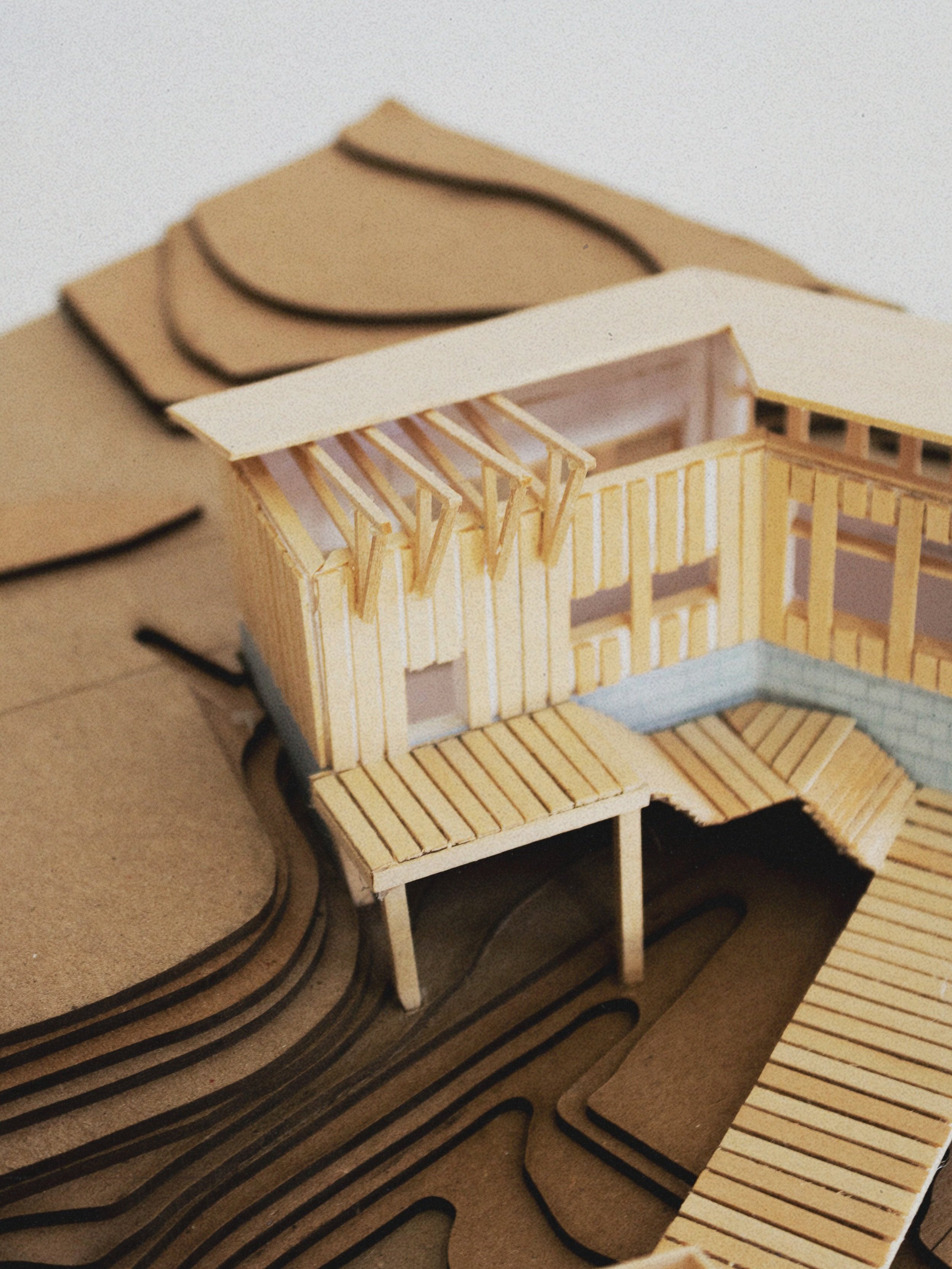 Architectural model of a house with a deck, made of paper and wood, on a layered topographical map.