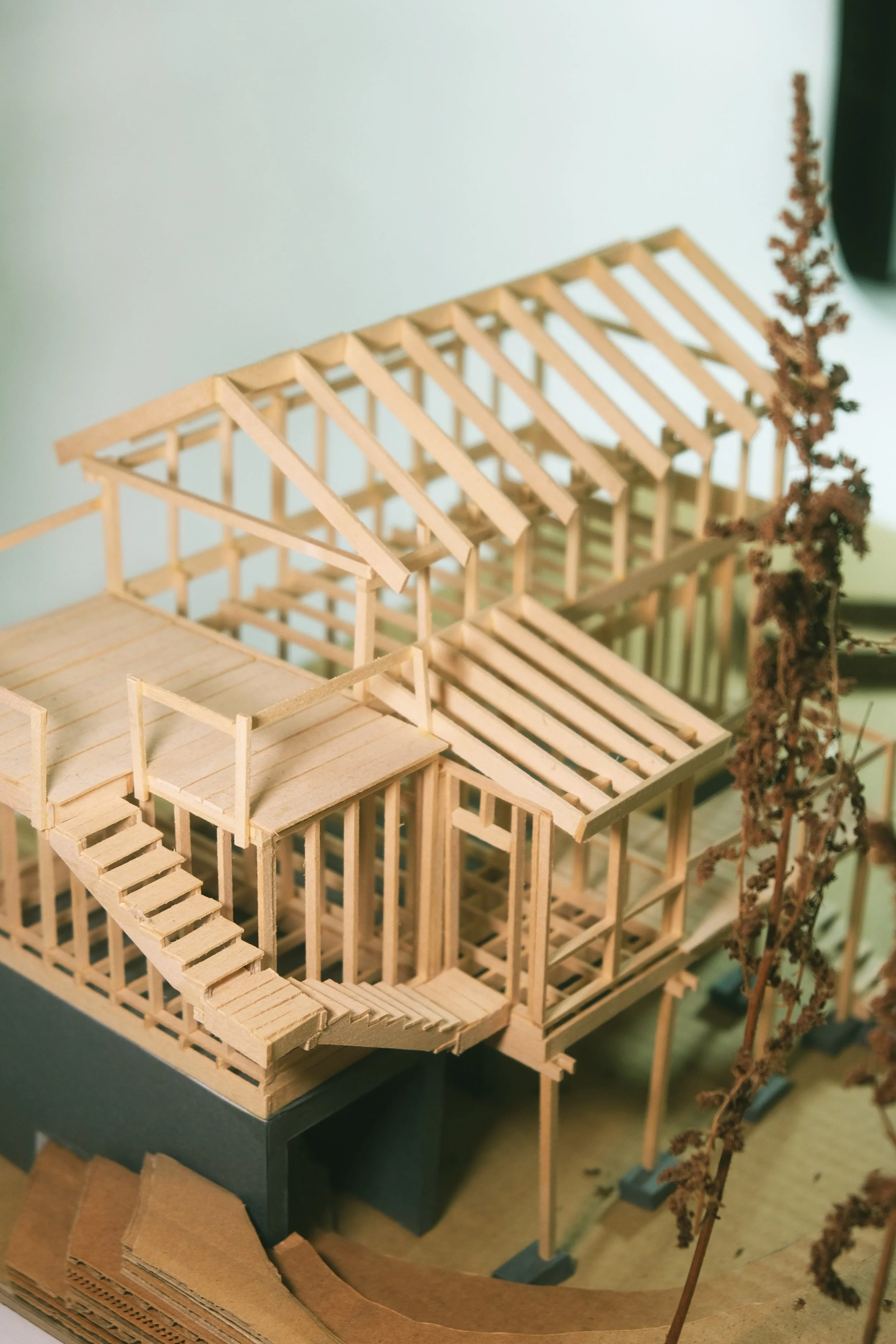 Wooden architectural model of a house under construction, featuring a staircase, open framework, and a roof in progress.