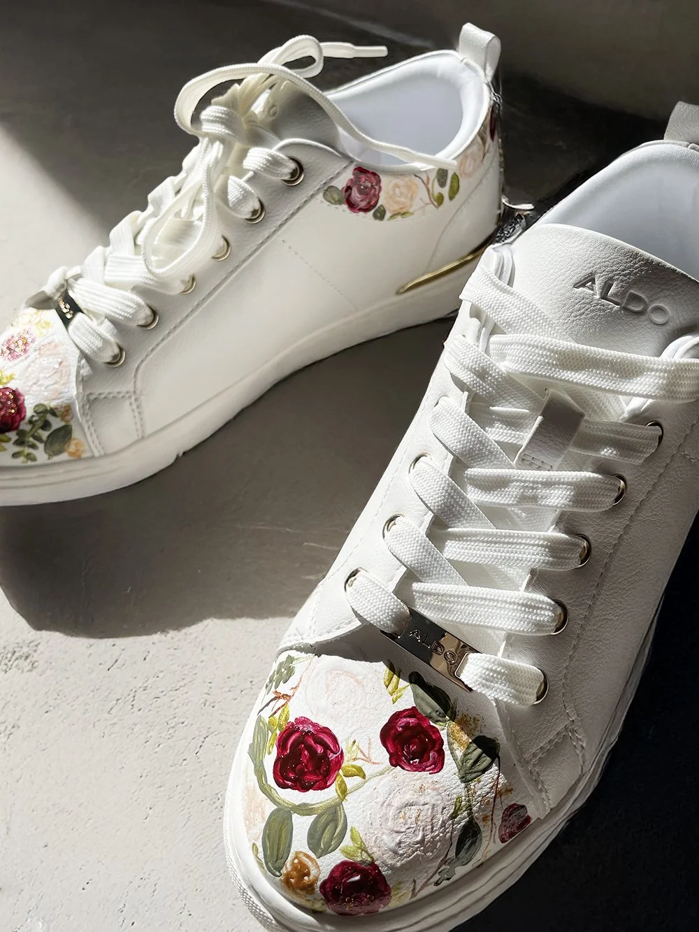 Close up image of white sneakers custom painted with abstract roses & leaf motifs