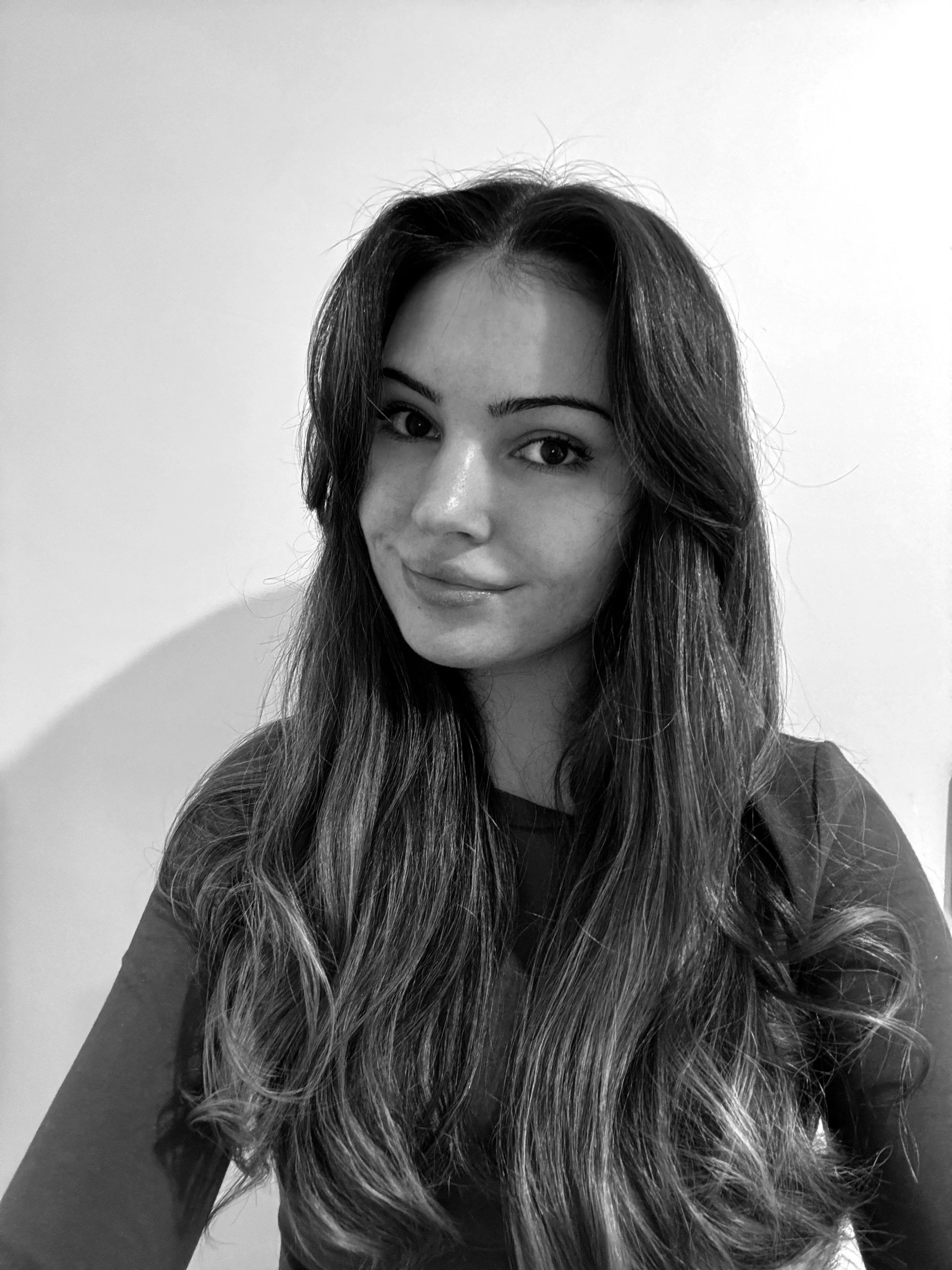 Black and white photo of a woman with long, wavy hair, smiling slightly, looking at the camera, against a plain background.