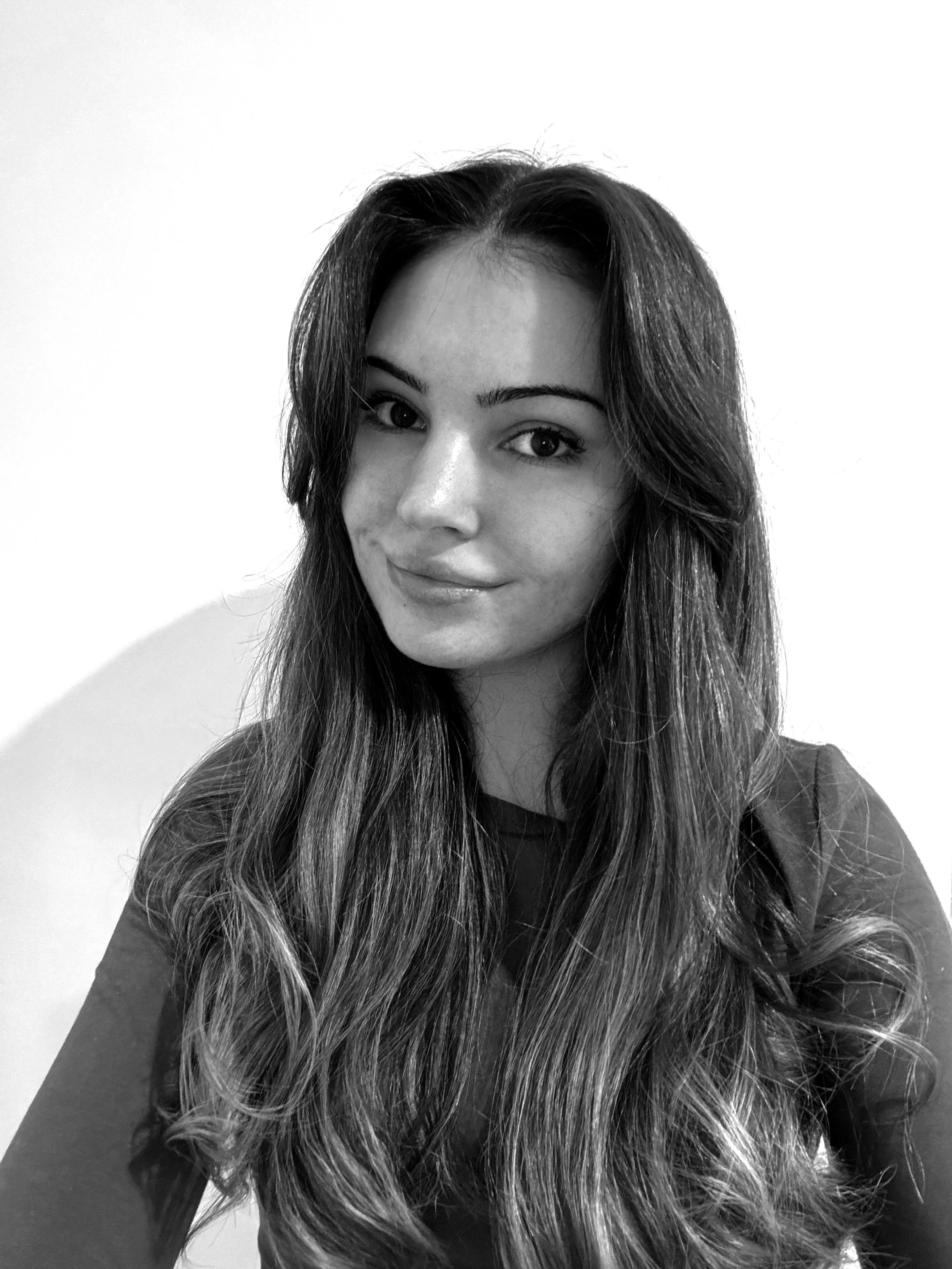 A black and white portrait of a woman with long, wavy hair, smiling slightly, against a plain background.