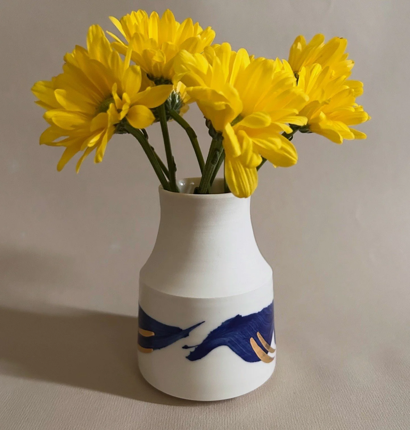 Yellow flowers in a white and blue vase on a beige surface.