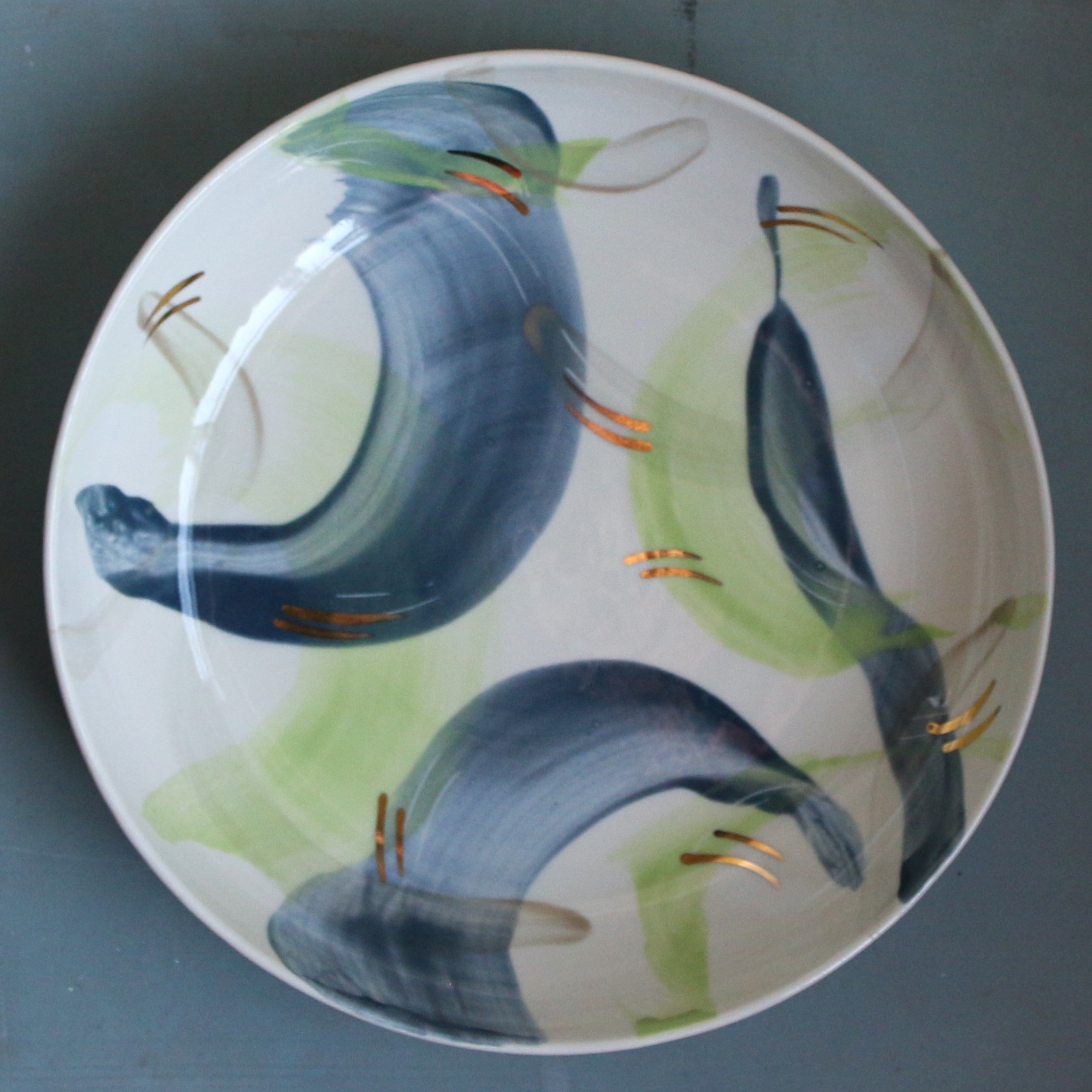 A decorated ceramic plate with abstract painted design featuring blue, green, and orange colors on a dark surface.