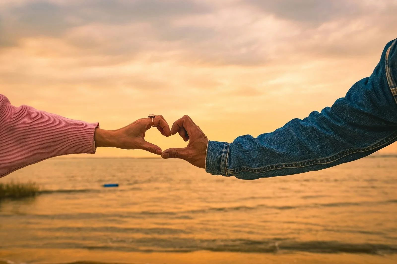 couple forming a heart with their hands  on a beach