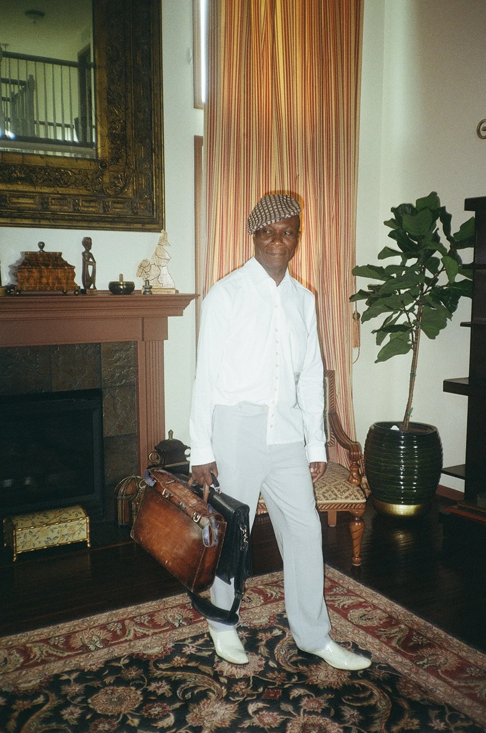 A man posing with two briefcases. Wearing a white shirt and blue trousers.