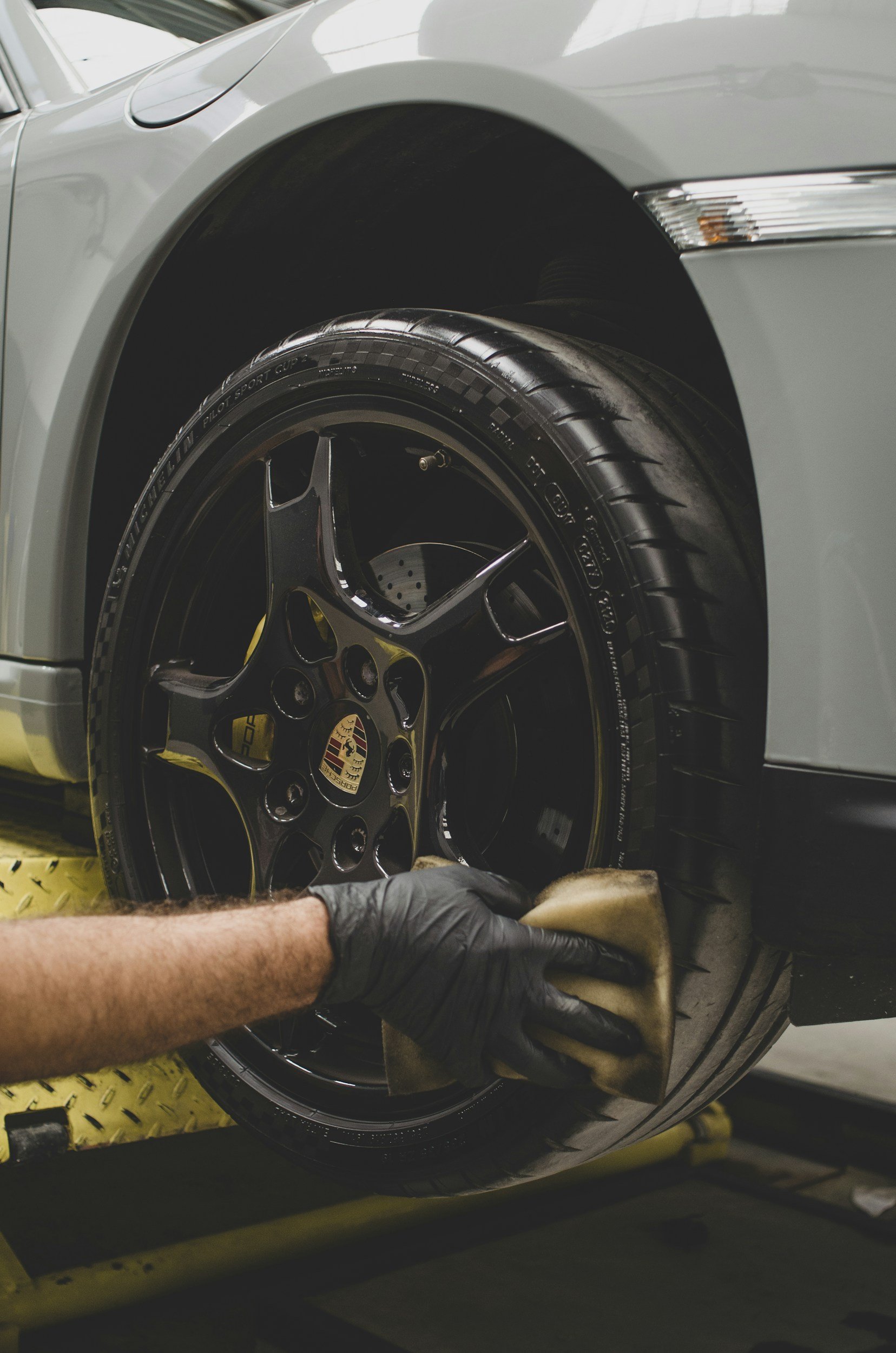 Person cleaning car tire with black rim, wearing black gloves