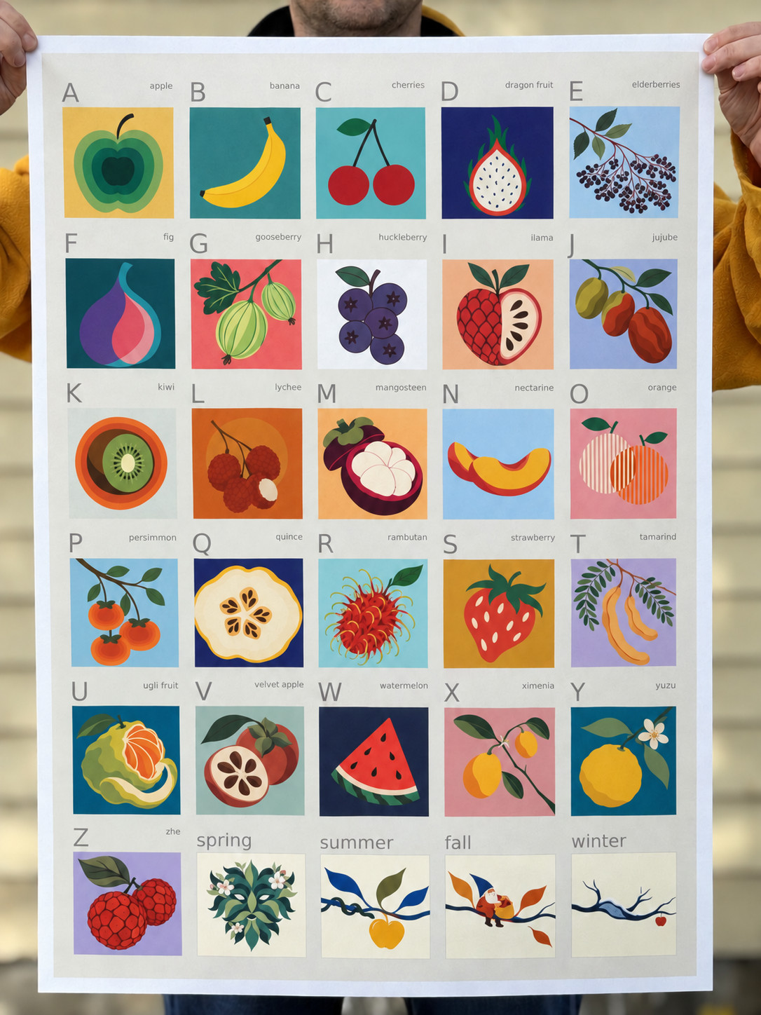 Fruit Alphabet poster held up in soft daylight, showing the colorful fruit grid and white border.