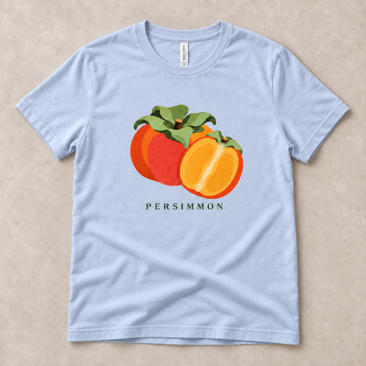 Light Blue Persimmon T-shirt with a whole orange persimmon, a golden cut half and green leaves printed on the front.