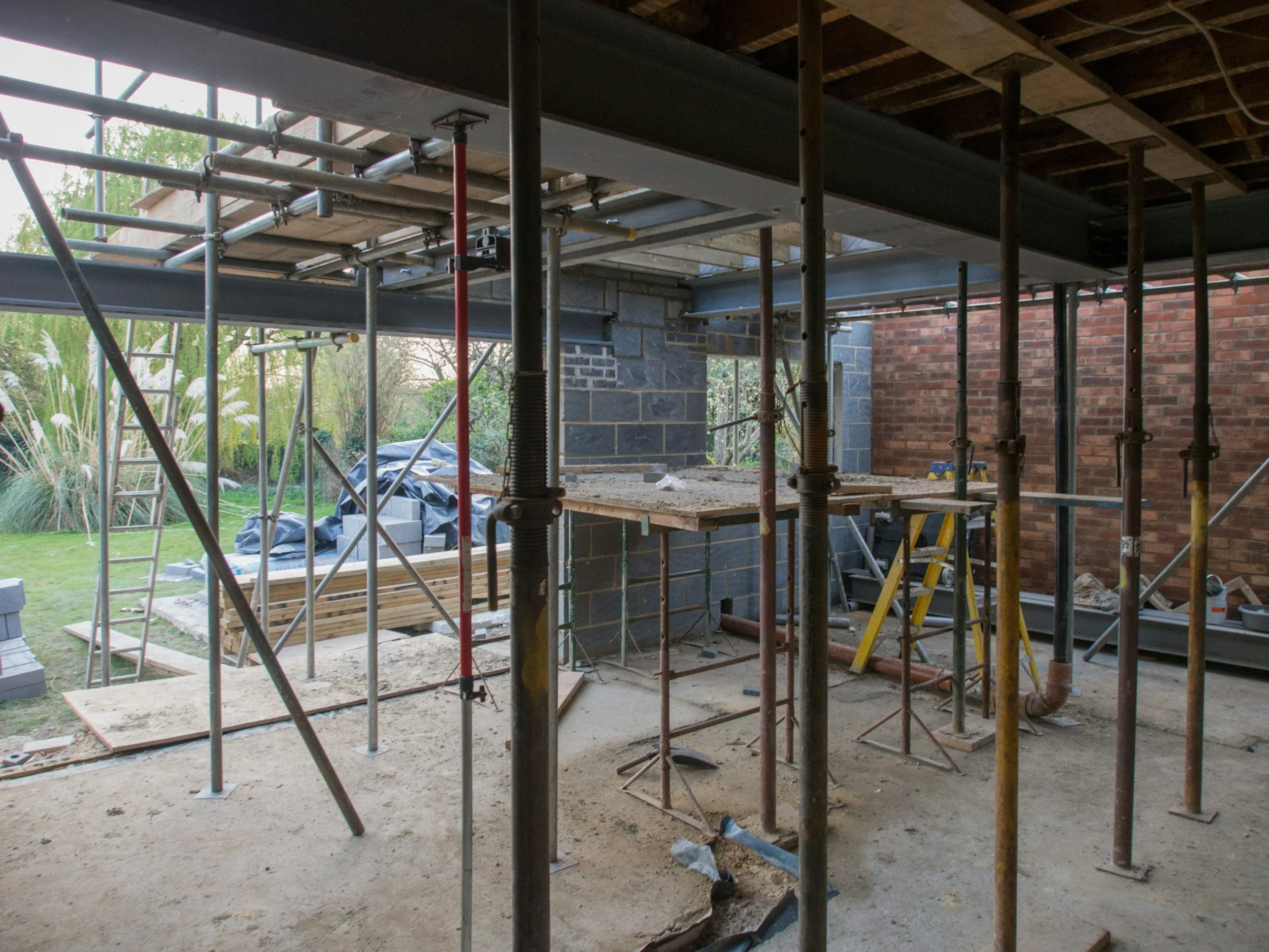 Construction site with scaffolding and building materials, including bricks, wood, and pipes, during house construction.